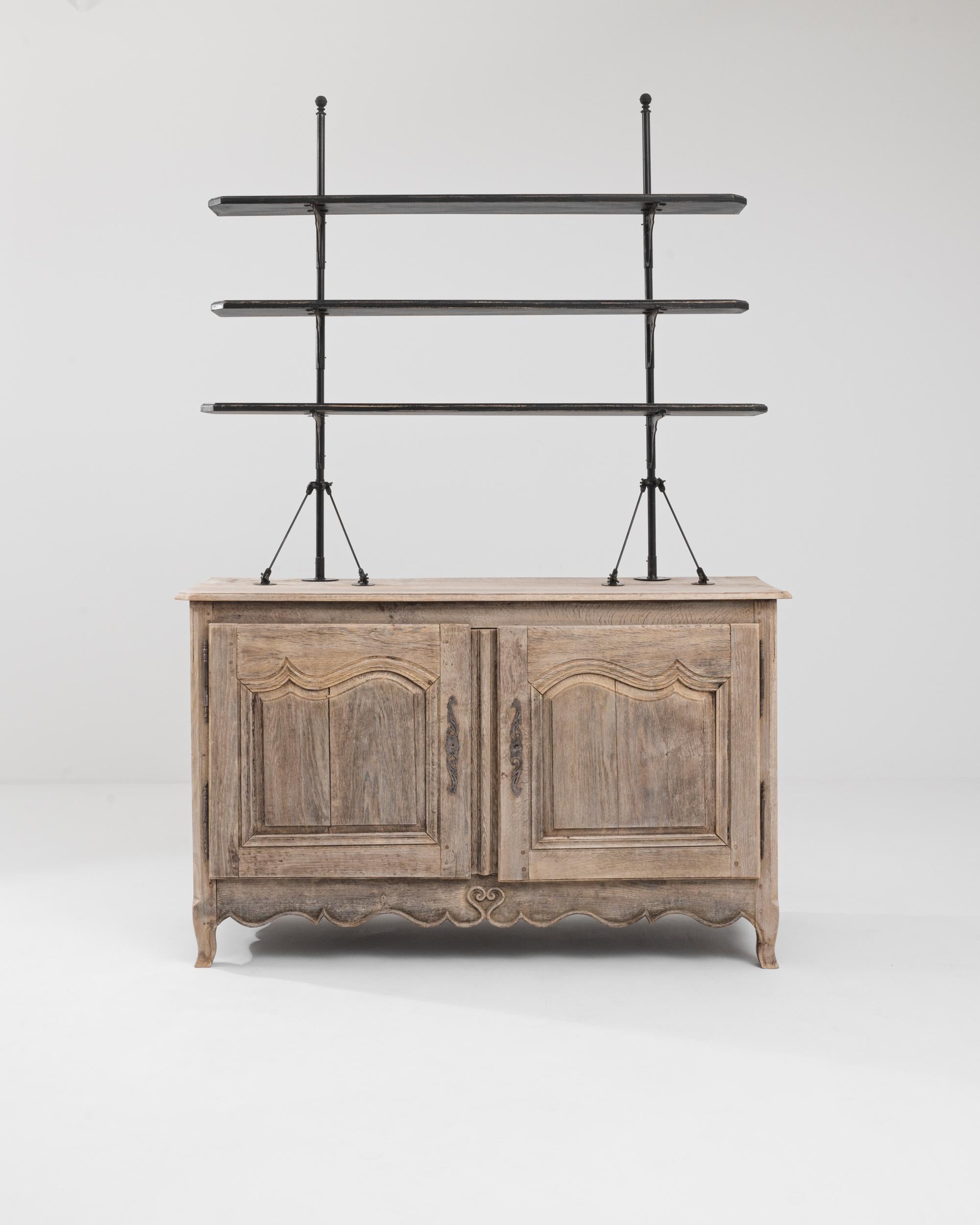 Graceful and unique, this antique oak display cabinet cuts a striking silhouette. Made in France in the 1800s, the light, airy design of the upper shelves evokes the masts of sailing ships; the paneling of the lower cabinet rises in crests like