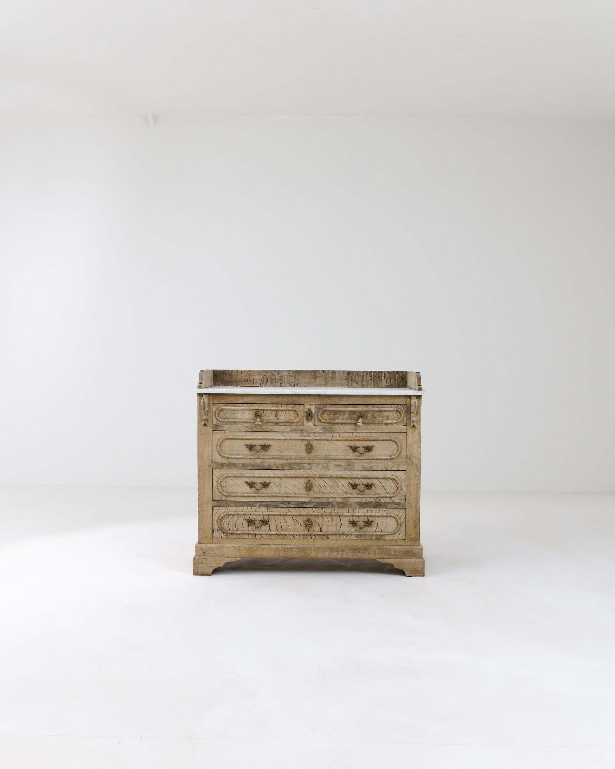 The sturdy bracket ogee feet define the silhouette of this robust antique chest. Its five drawers showcase meticulously crafted brass handles and lock pieces, adorned with foliate motifs that resonate in the carved details on the sides. The white