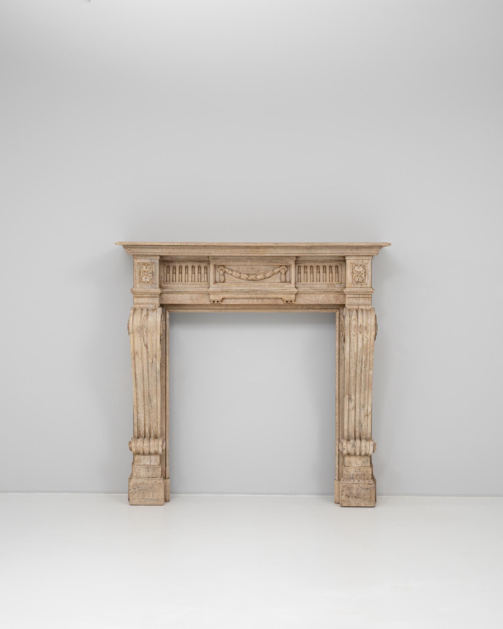 This 19th Century French oak fireplace showcases exquisite neoclassical craftsmanship with richly carved architectural details. The surround features fluted legs with volute capitals, rising to a deeply molded mantel shelf. The frieze is adorned