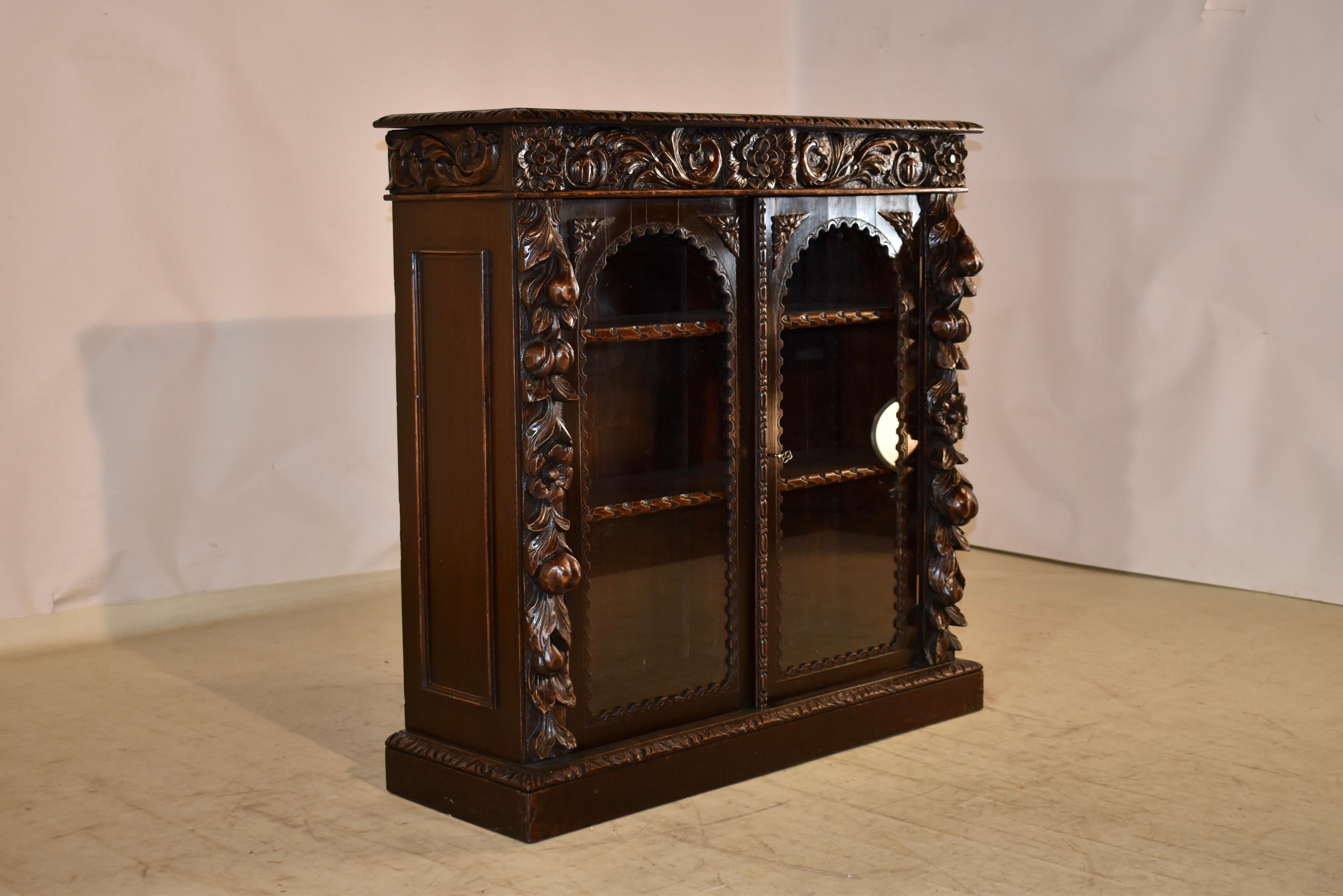 19th century oak bookcase from France with glazed doors.  The top is made from a single board and has a beveled and hand carved decorated edge.  This follows down to a gloriously hand carved apron.  The apron is over simple sides which have added