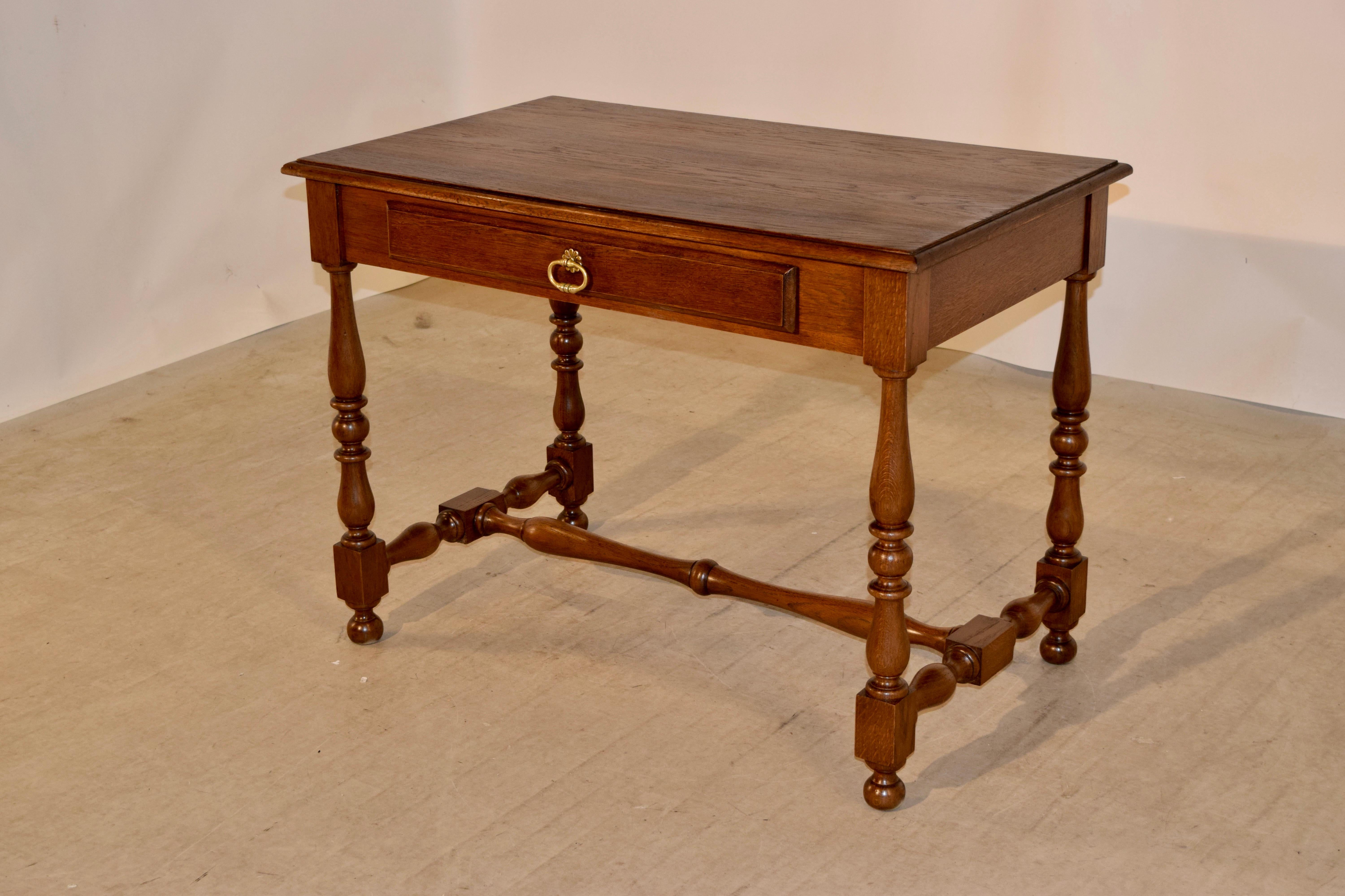 19th century oak library table from France with a bevelled edge around the top, following down to a simple apron containing a single drawer in the front. The piece is supported on hand turned legs, joined by a hand turned stretcher and raised on