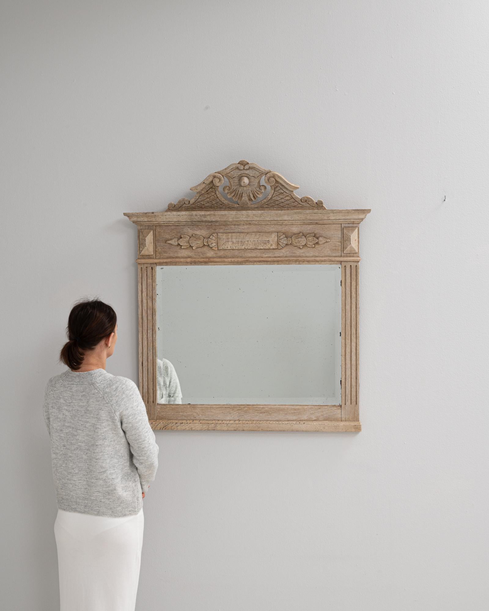 This 19th century French oak mantel-style mirror features finely carved detailing that reflects Neoclassical influences. The crest showcases an elegant central shell motif flanked by scrolling acanthus elements and latticework panels, lending a
