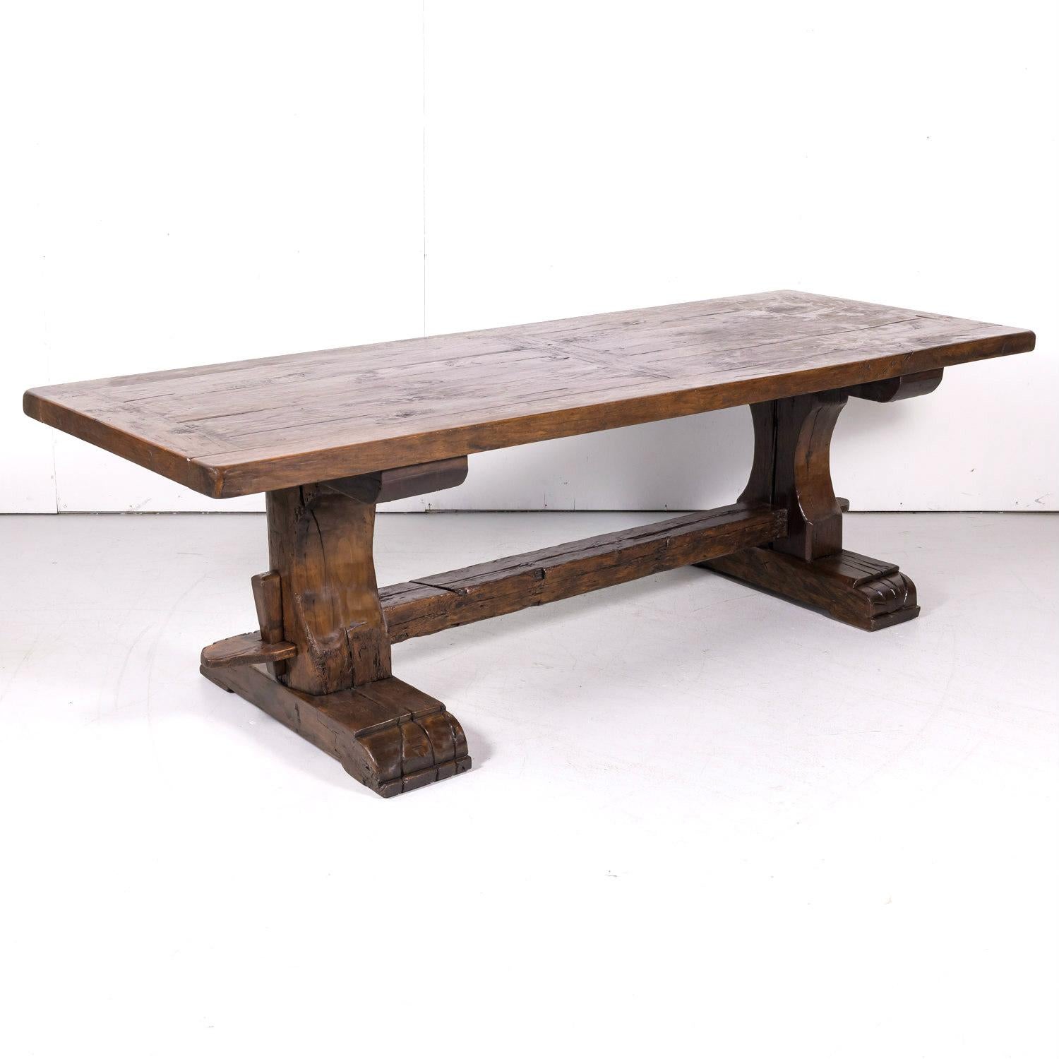 A 19th century French monastery trestle table handcrafted in Provence near Avignon of old growth French oak, circa 1890s. Having a banded plank top supported by carved trestle legs on plinth bases, each joined by a thick center stretcher, circa