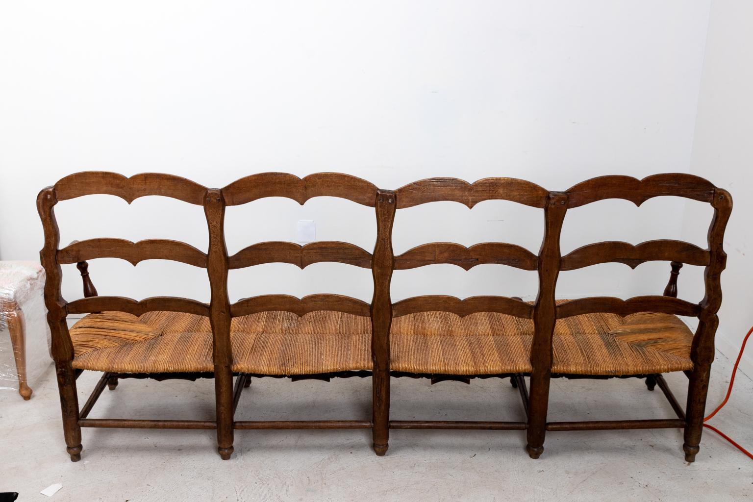 French oakwood settee with woven rushed seat and slat back, circa 19th century. The piece also features carved floral detail on the curved skirt and bottom turned stretcher. Please note of wear consistent with age including minor finish loss to the