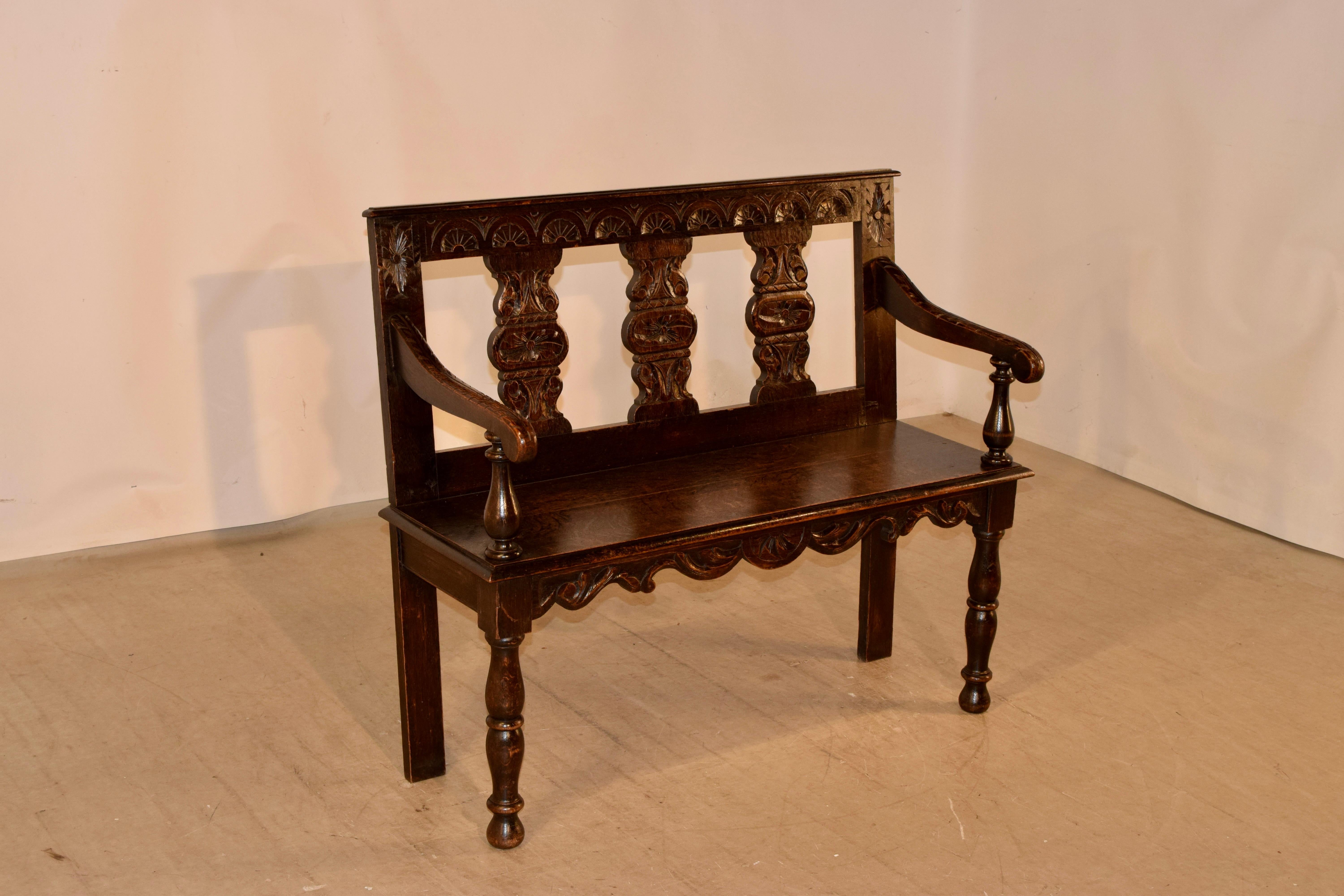 19th century French settee made from oak. The back is carved and has three vase shaped carved panels, following down to a seat with a bevelled edge along the front, and turned arms. The legs are hand-turned in the front and simple in the back for