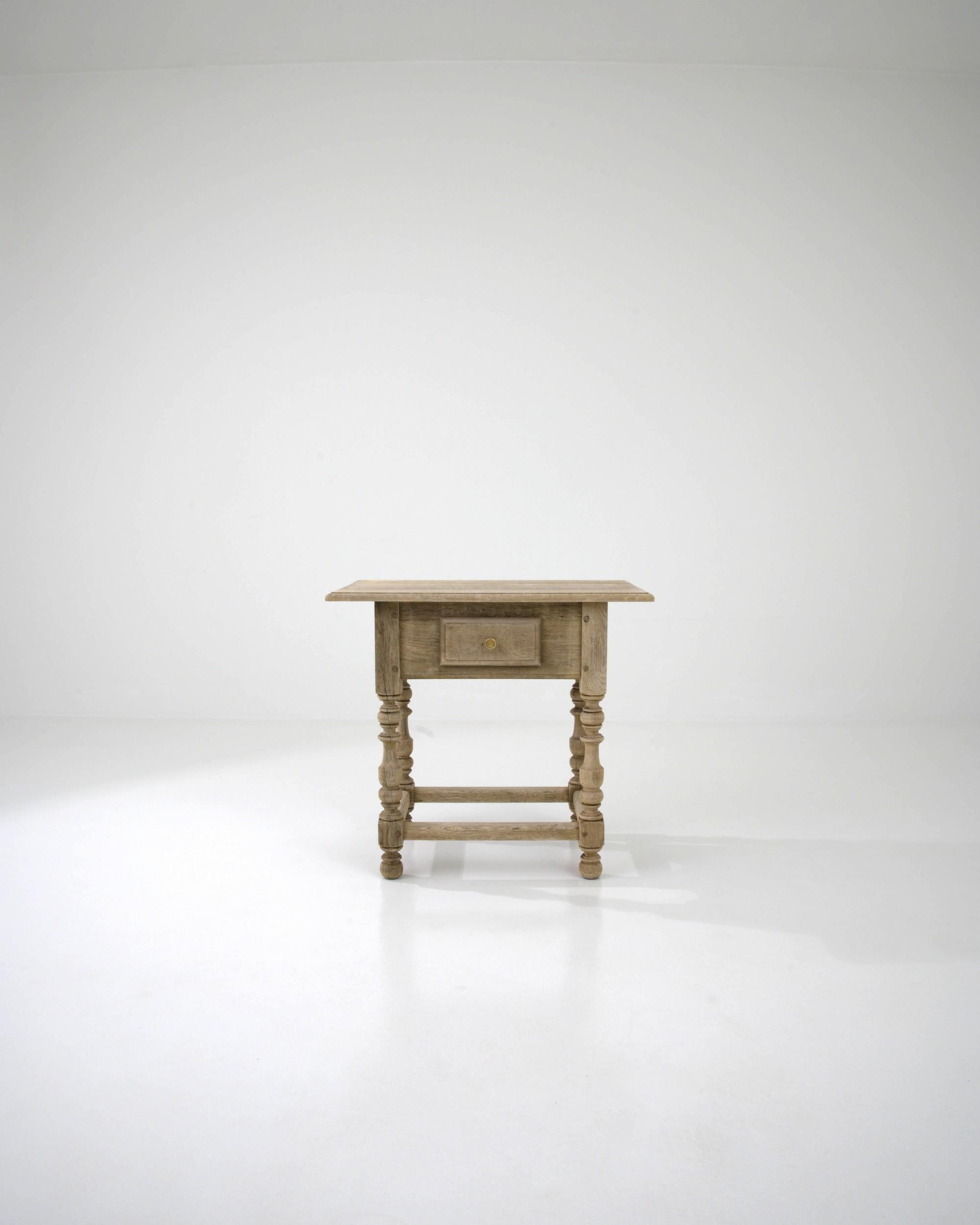 Radiating rustic charm, enhanced by the ashen finish of the bleached oak wood, this 19th-century French side table is a testament to craftsmanship. Its carved elements, including a scalloped apron and baluster legs, supported by bun feet and