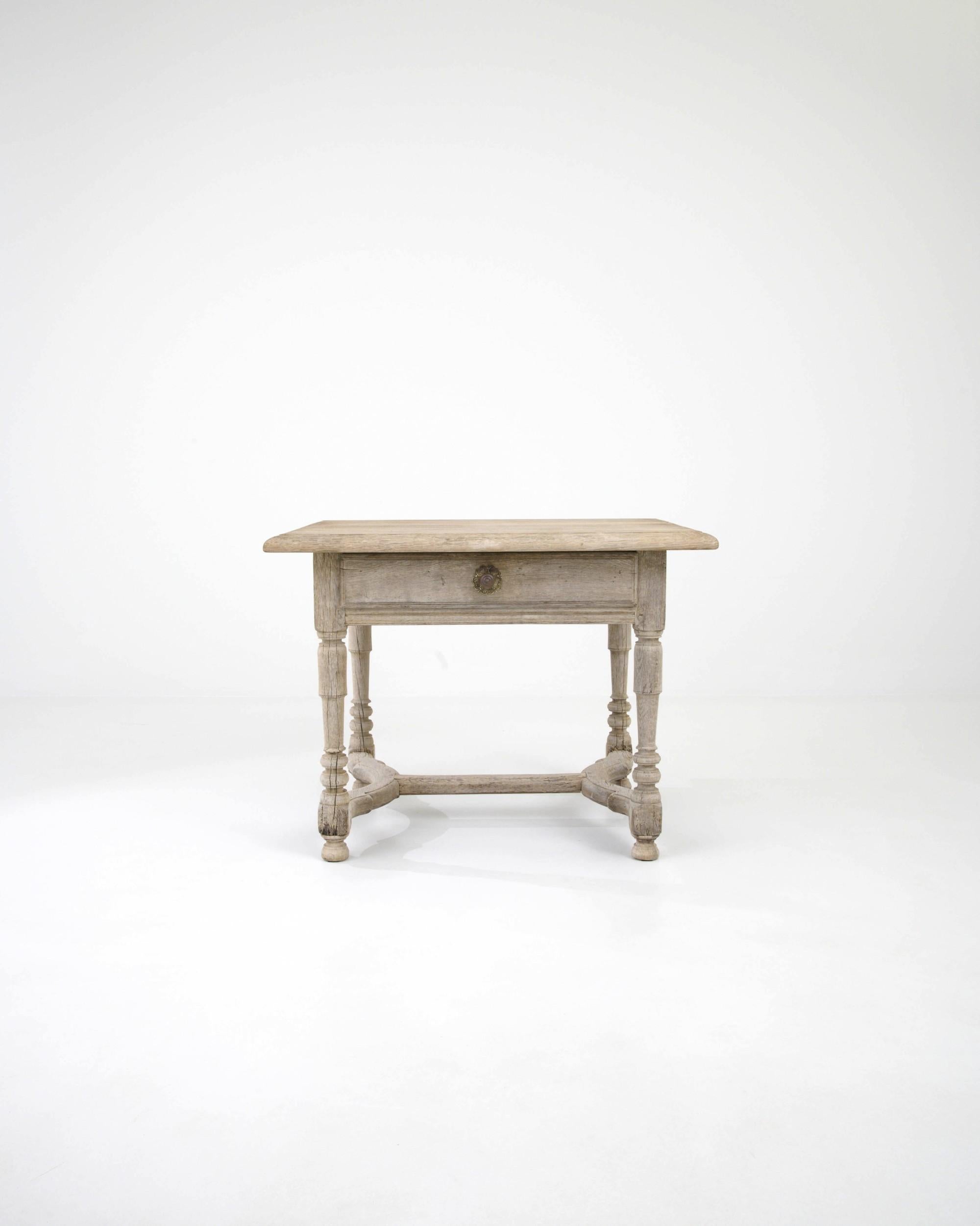 Radiating rustic charm, enhanced by the ashen finish of the bleached oak wood, this 19th-century French side table is a testament to craftsmanship. Its carved elements, including a scalloped apron and baluster legs, supported by bun feet and