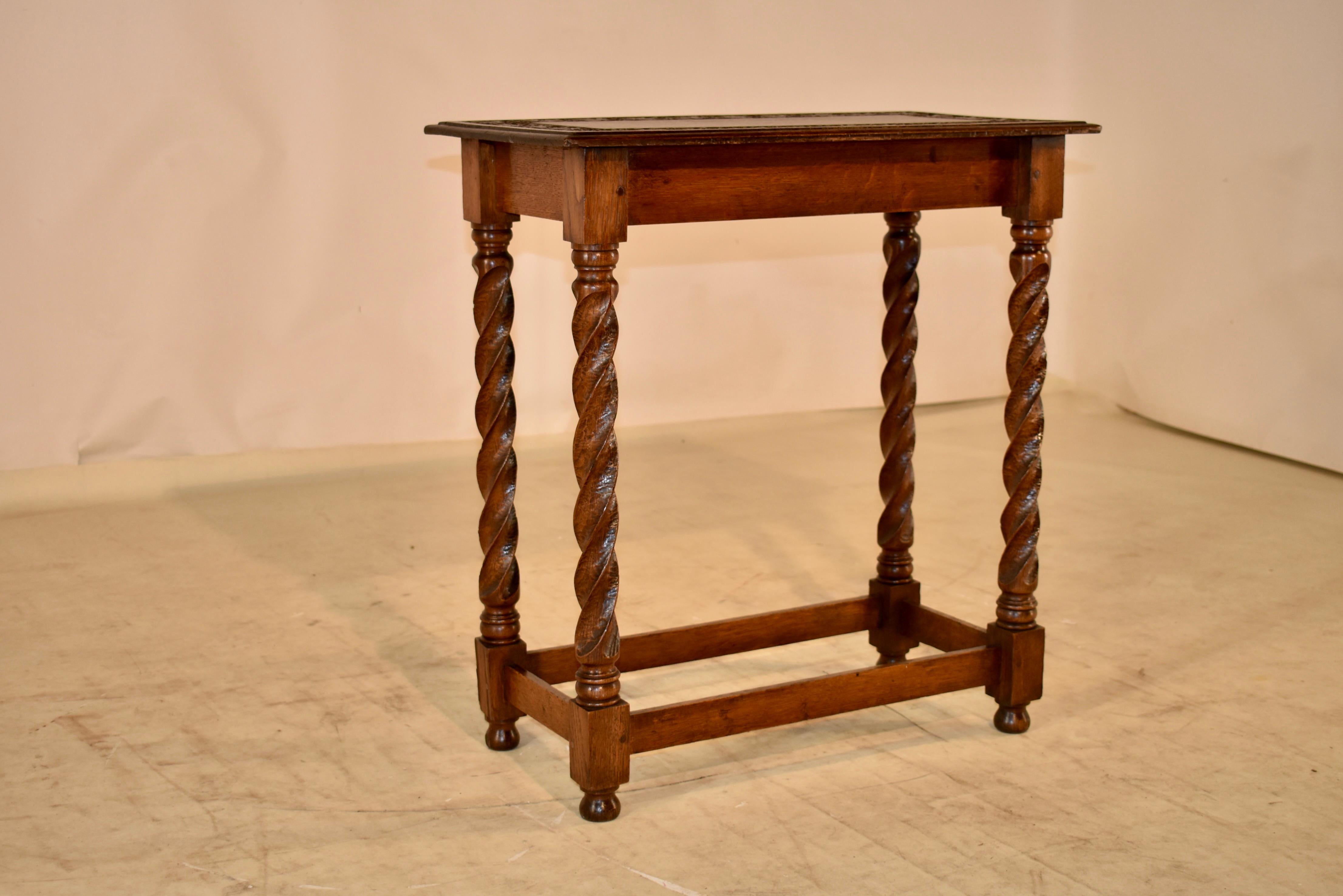 19th century oak side table from France with a hand carved banding on the top, depicting lovely leaves and a beveled edge. The apron is simple, and the table is supported on hand carved ribbon twist legs, joined by simple stretchers and raised on