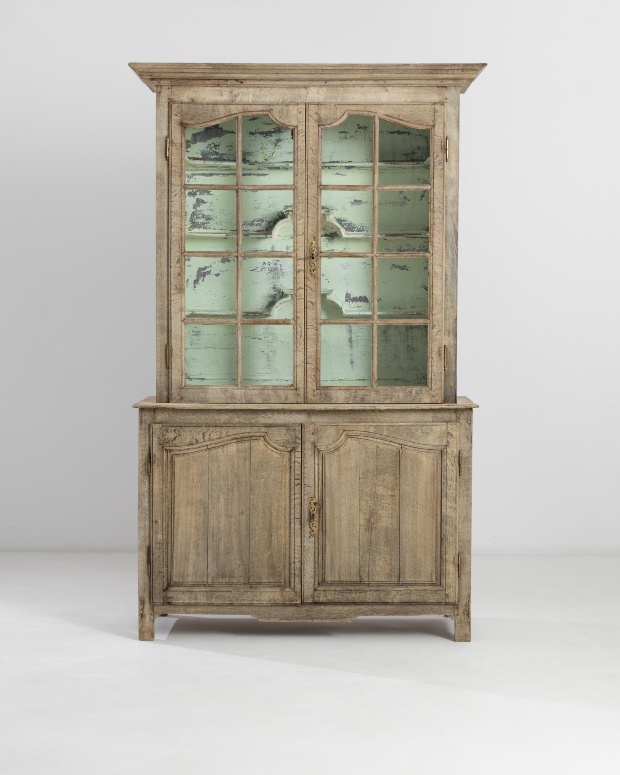 Hand-crafted in 19th century France, this oak vitrine presents a classical ‘deux corps’ anatomy. The glazed doors in the upper section reveal a refreshing light green finish of the interior with three built-in shelves. The lower cupboard with a