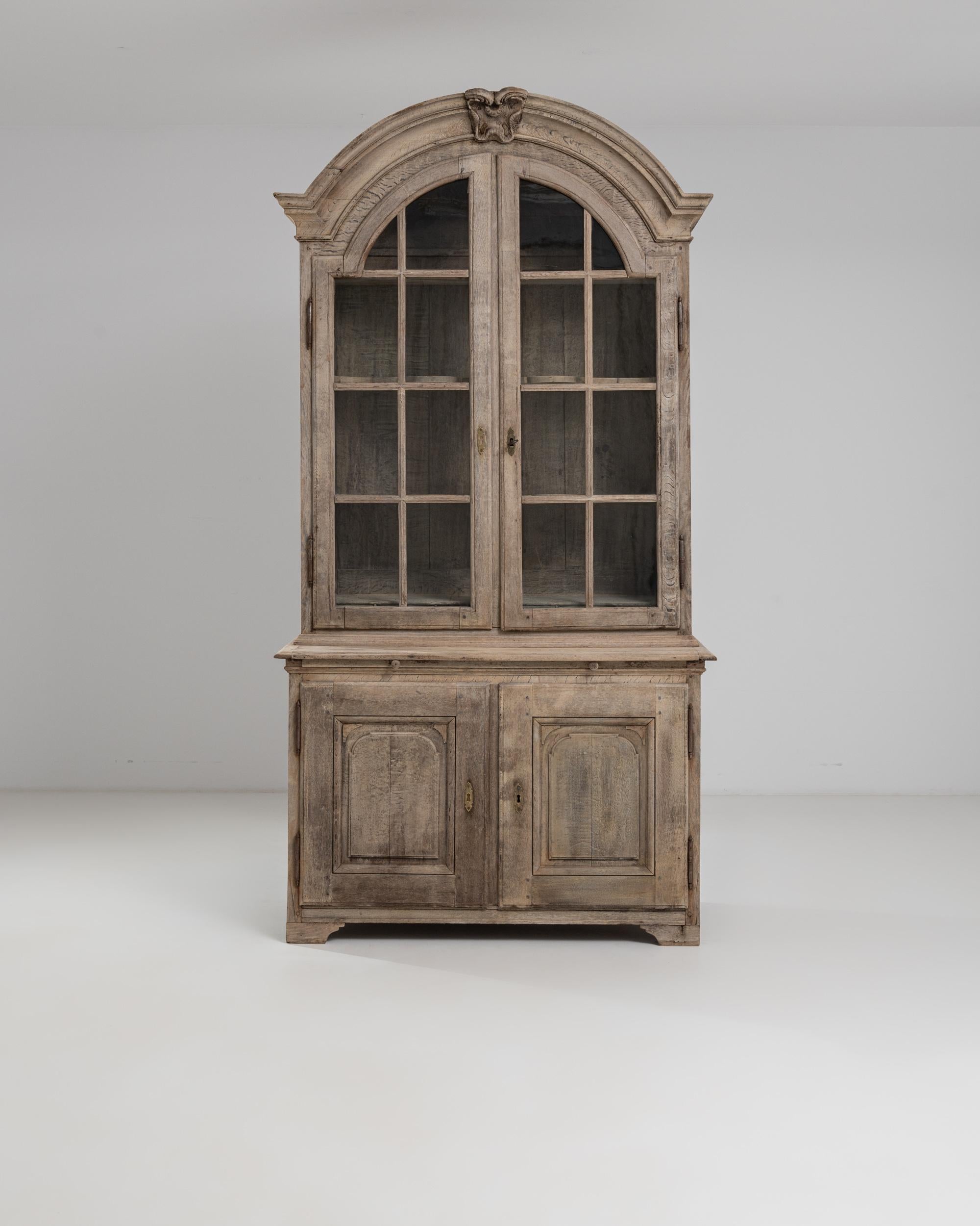 This delightful French provincial oak vitrine combines Neoclassical and rustic elements to elegant effect. Made in 19th Century France, the molded arch of the upper cabinet creates a grand architectural silhouette; mullioned windows open out onto