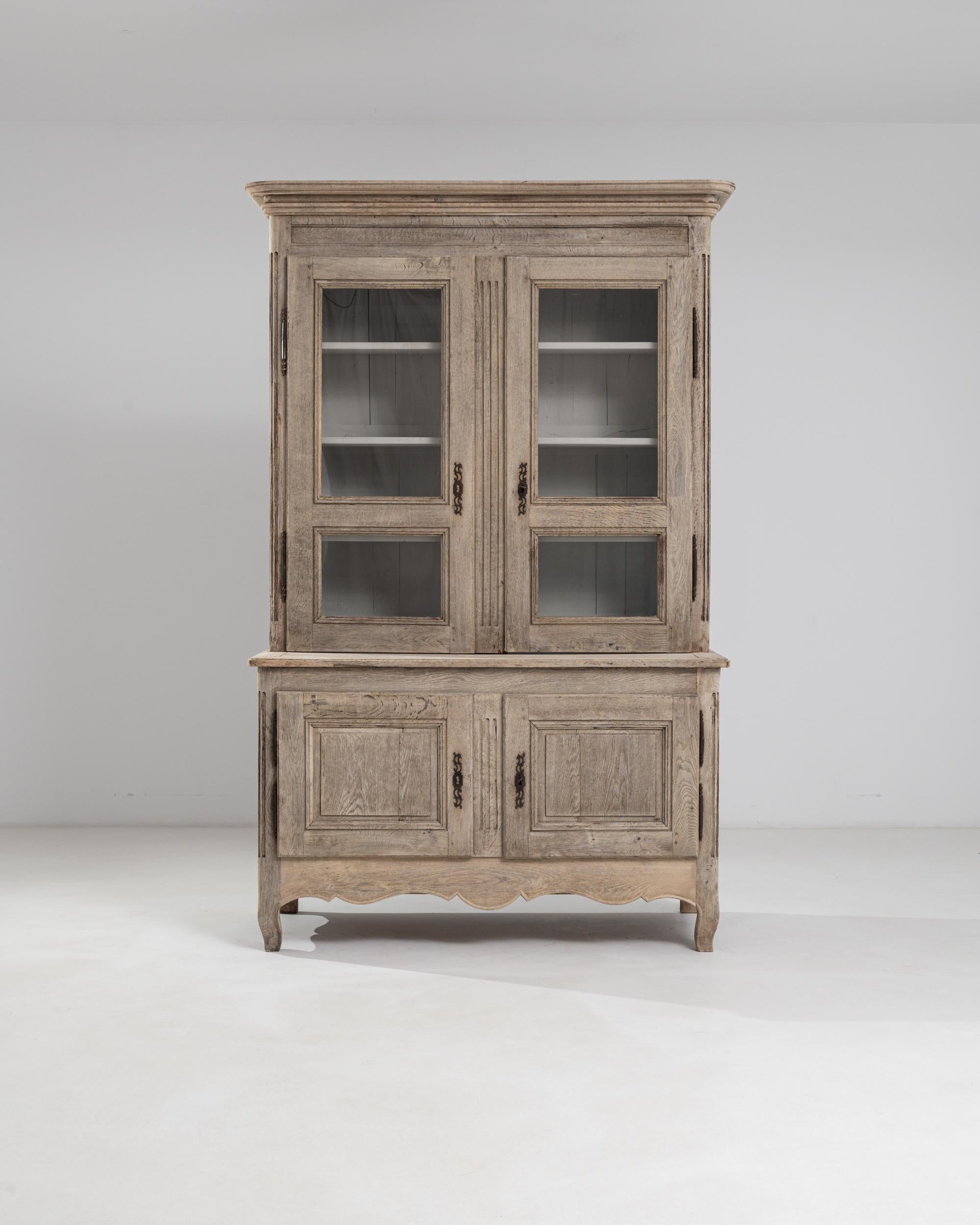 A 19th century wooden vitrine produced in France, this tall vitrine stands on cabriole feet and elevates above seven feet and a half. Provided with a scalloped apron and a molded cornice, the two-case piece is composed of a large four-shelf vitrine