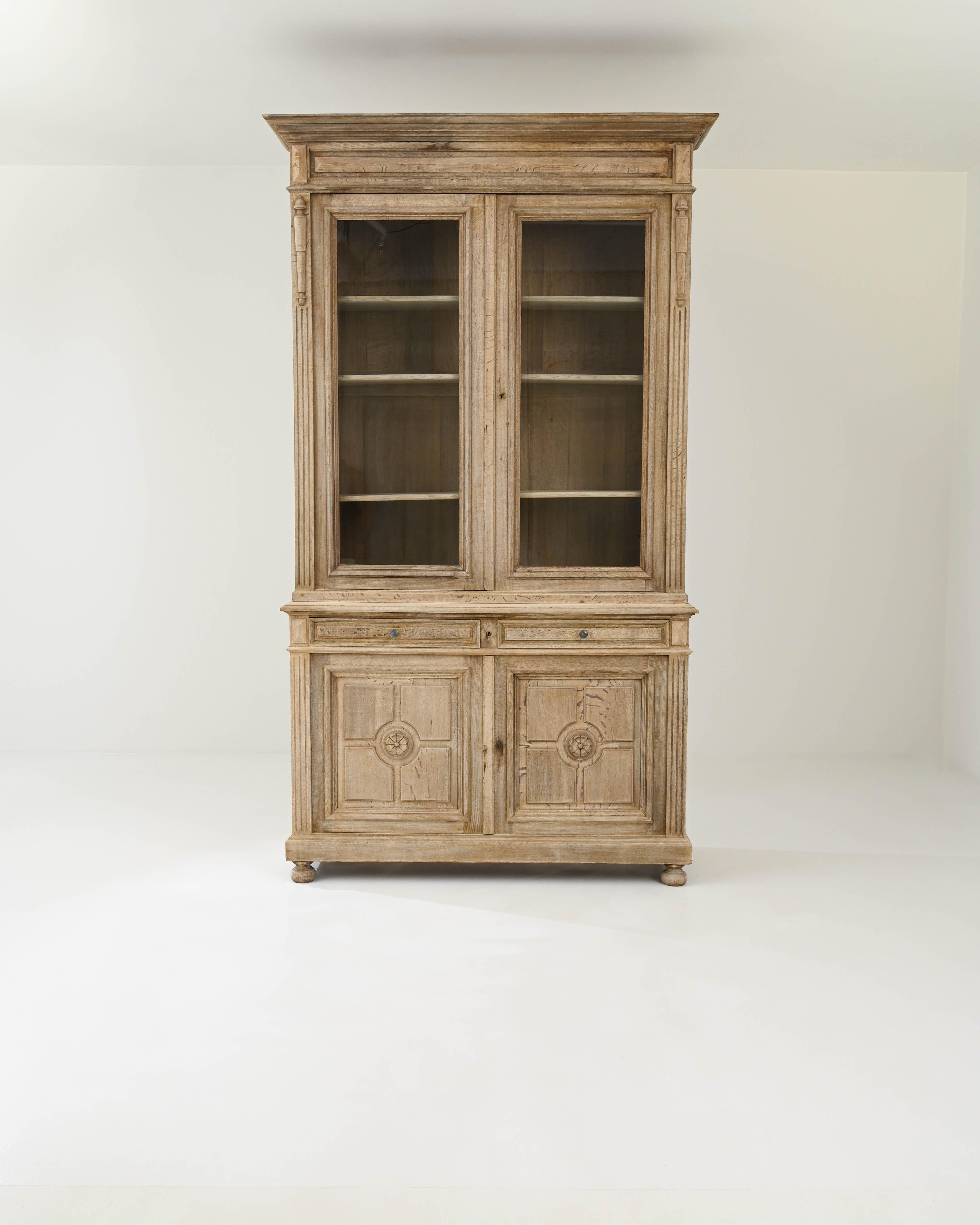 The impressive stature and Neoclassical refinement of this antique oak vitrine make it a sight to behold. Built in France in the 1800s, the tall cabinet is crowned by a carved cornice, giving the piece an architectural quality. The windows of the