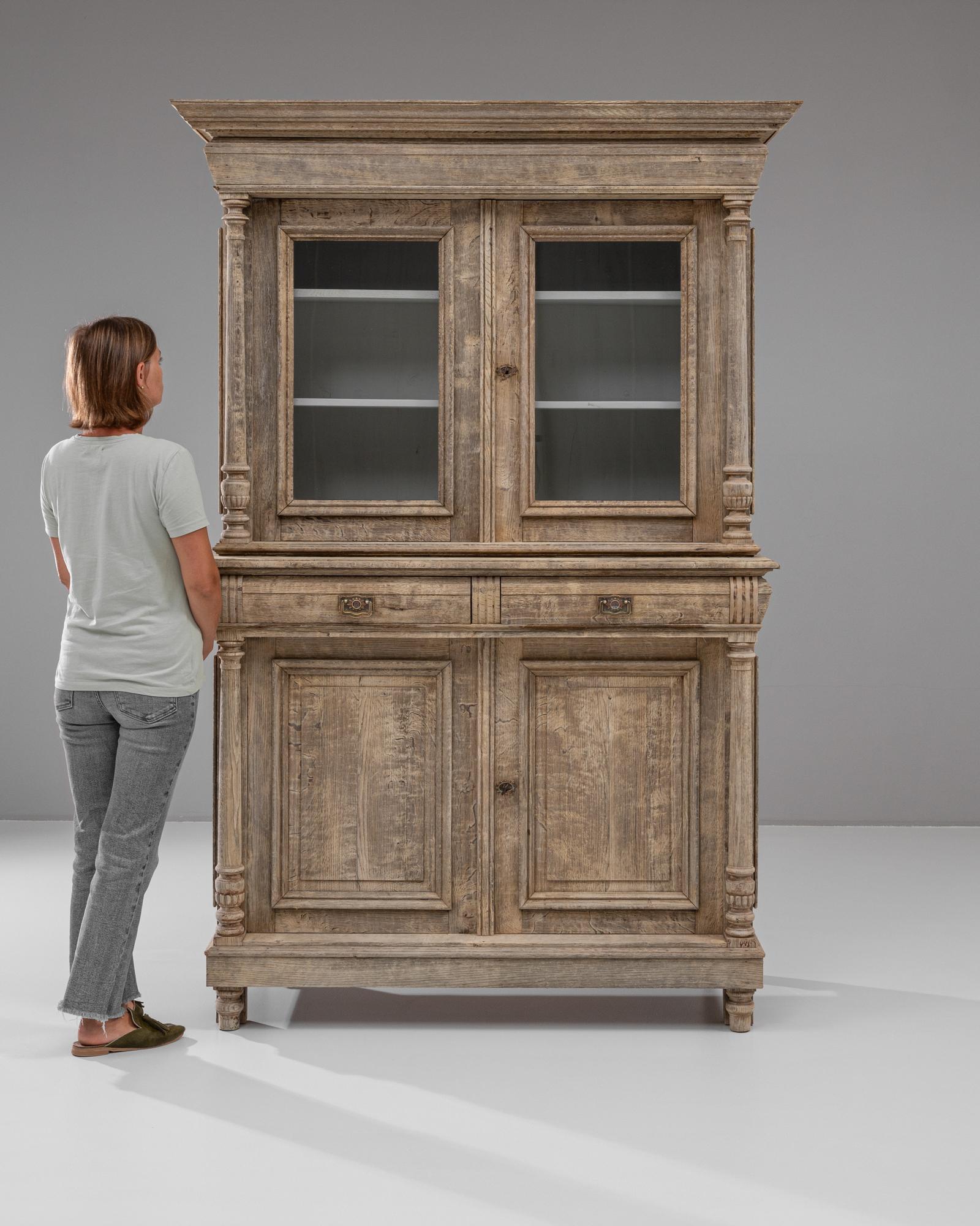 Questa vetrina in rovere francese del XIX secolo è una miscela magistrale di eleganza e funzionalità, che mette in mostra un'eccezionale maestria artigianale. La robusta struttura in Oak è completata da intricati dettagli intagliati, tra cui colonne