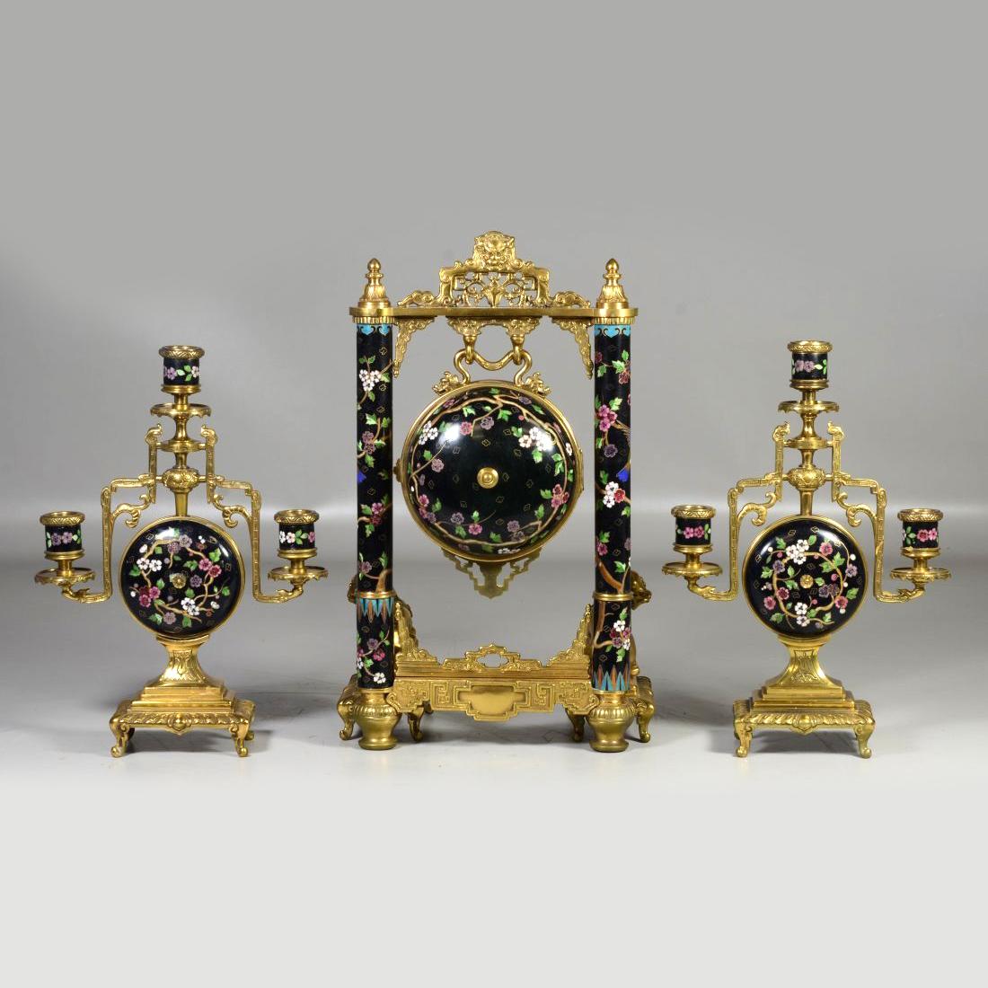 A fine chinoiserie gilt bronze and cloisonne three-piece clock set by Japy Freres.
The ball encased movement hanging as a gong from a frame with bronze Chinese elements and cloisonne columns, with foodog supports with a pair of matching