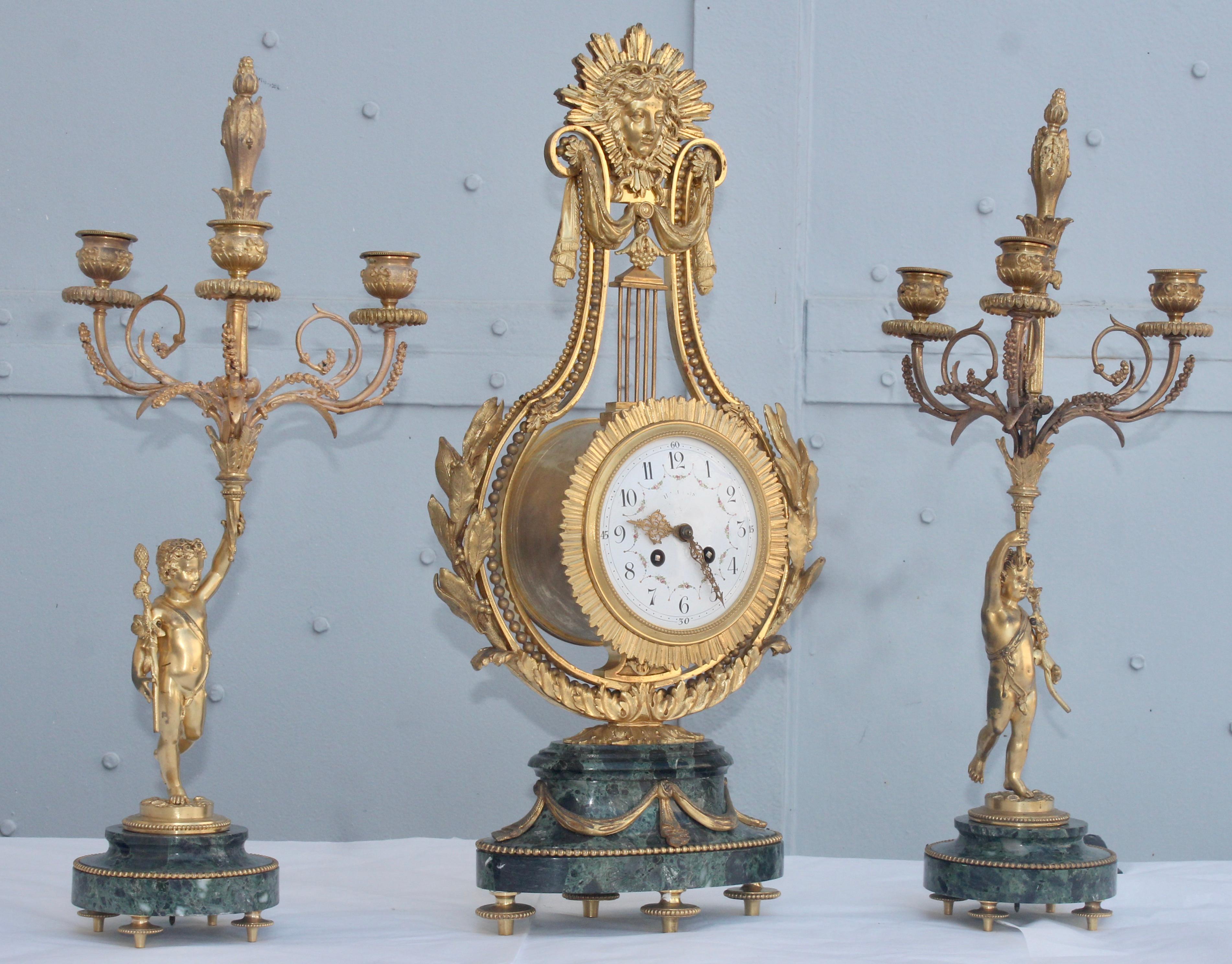 A 19th century French Ormolu and Vert de Mer marble three-piece lyre clock garniture
The central clock is shaped as a lyre, and mounted all over with gilt bronze leaves and swags, surmounted by a sun mask on both sides, resting on green marble oval