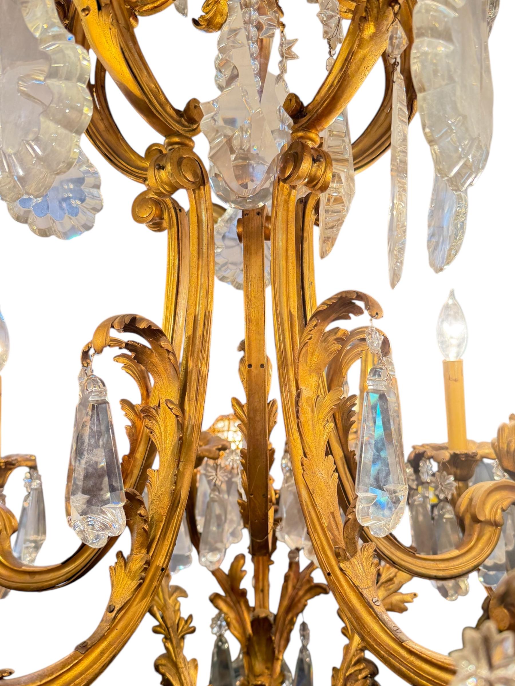 Eleva qualsiasi interno con questo opulento lampadario francese del XIX secolo, magistralmente realizzato in bronzo dorato e ormeggiato con prismi di cristallo sfaccettati a cascata. L'elaborata cornice di ispirazione rococò presenta ampie foglie