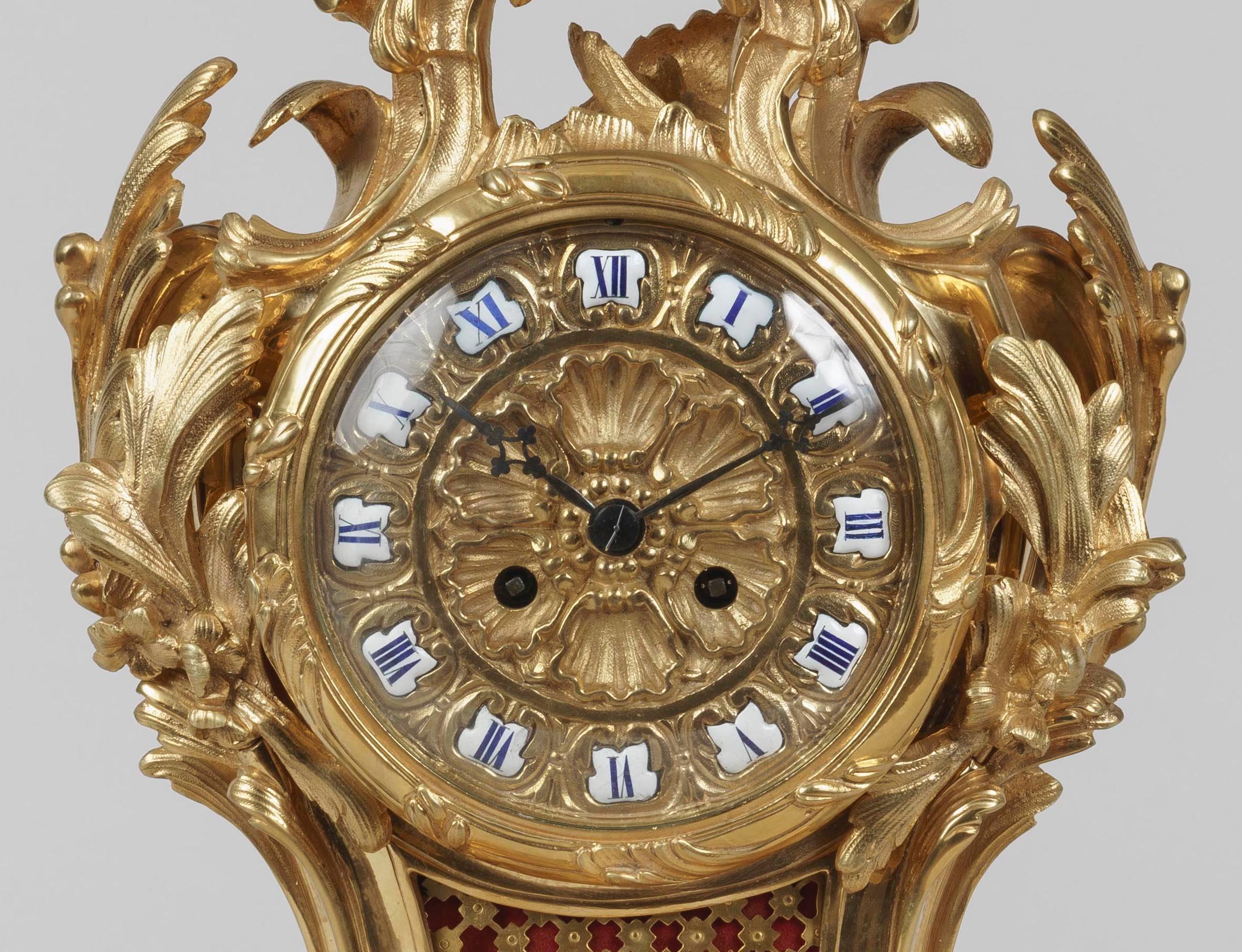 An Elegant Mantle Clock
In the Louis XV Manner

The clock and its plinth executed in gilt bronze in a dynamic rococo style, rising from scrolling foliage, the dial in the shape of a flower and having the hours marked by hand-painted porcelain roman