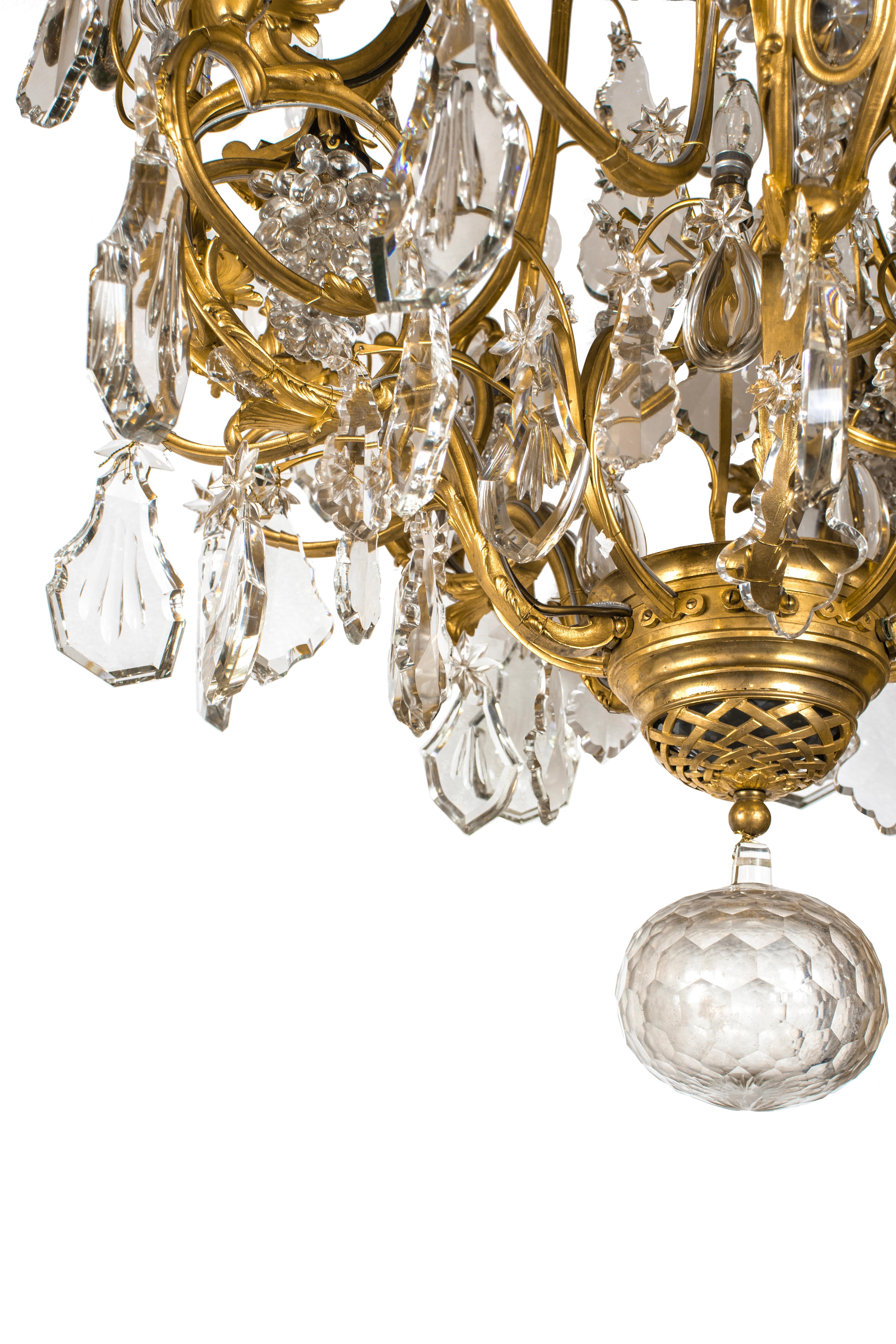 A large ormolu chandelier of Louis XV style with 10 lights on scrolling branches and one additional light bulb in the center. Decorated with oversized crystals of various shapes: stars, drops, rosettes, cones, curved prisms, and bunches of grapes.