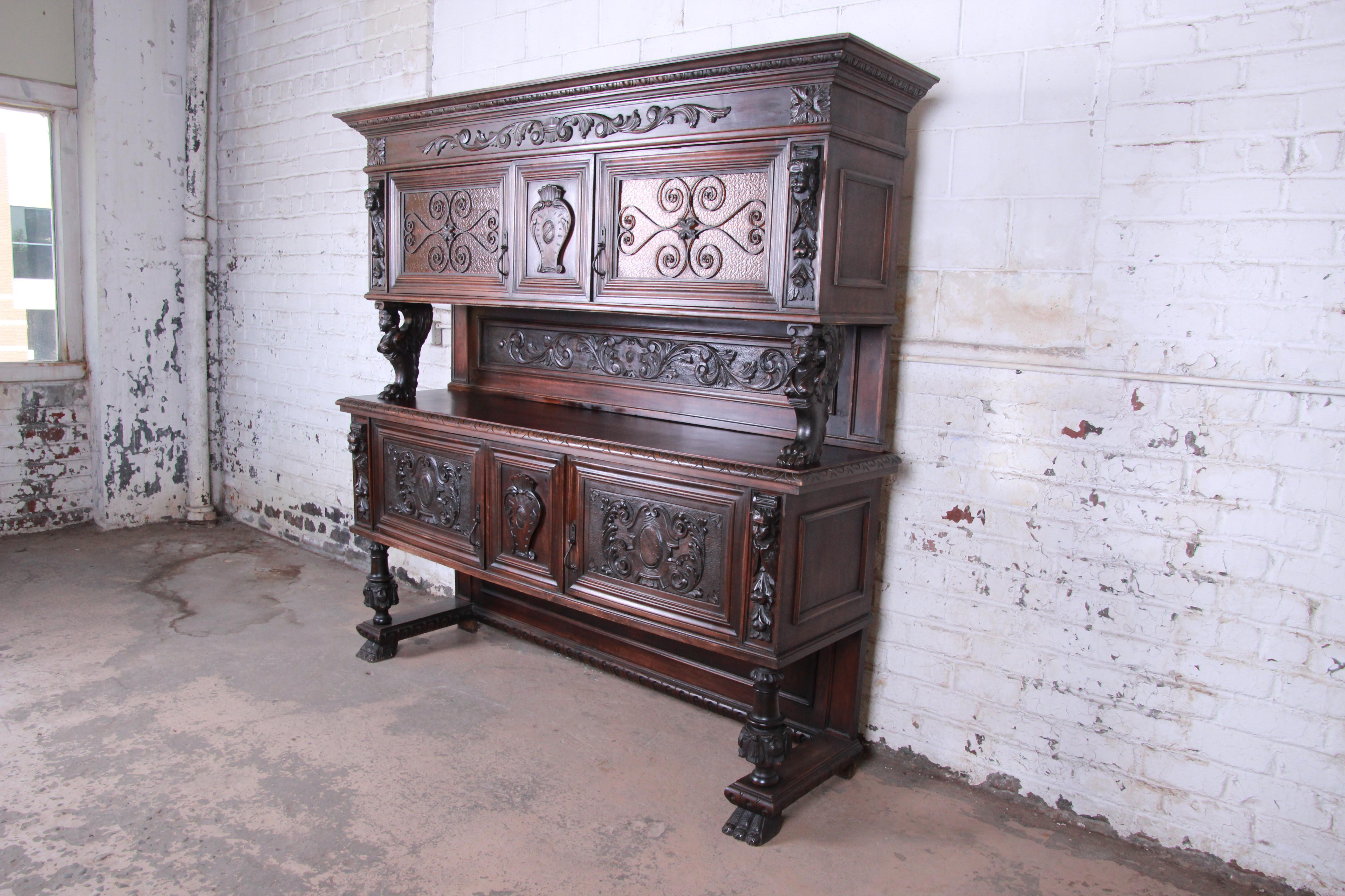 An outstanding 19th century French ornate carved walnut sideboard or bar cabinet. This outstanding cabinet features solid dark walnut construction with incredible carved wood details. It offers ample storage, with two cabinets behind stained glass