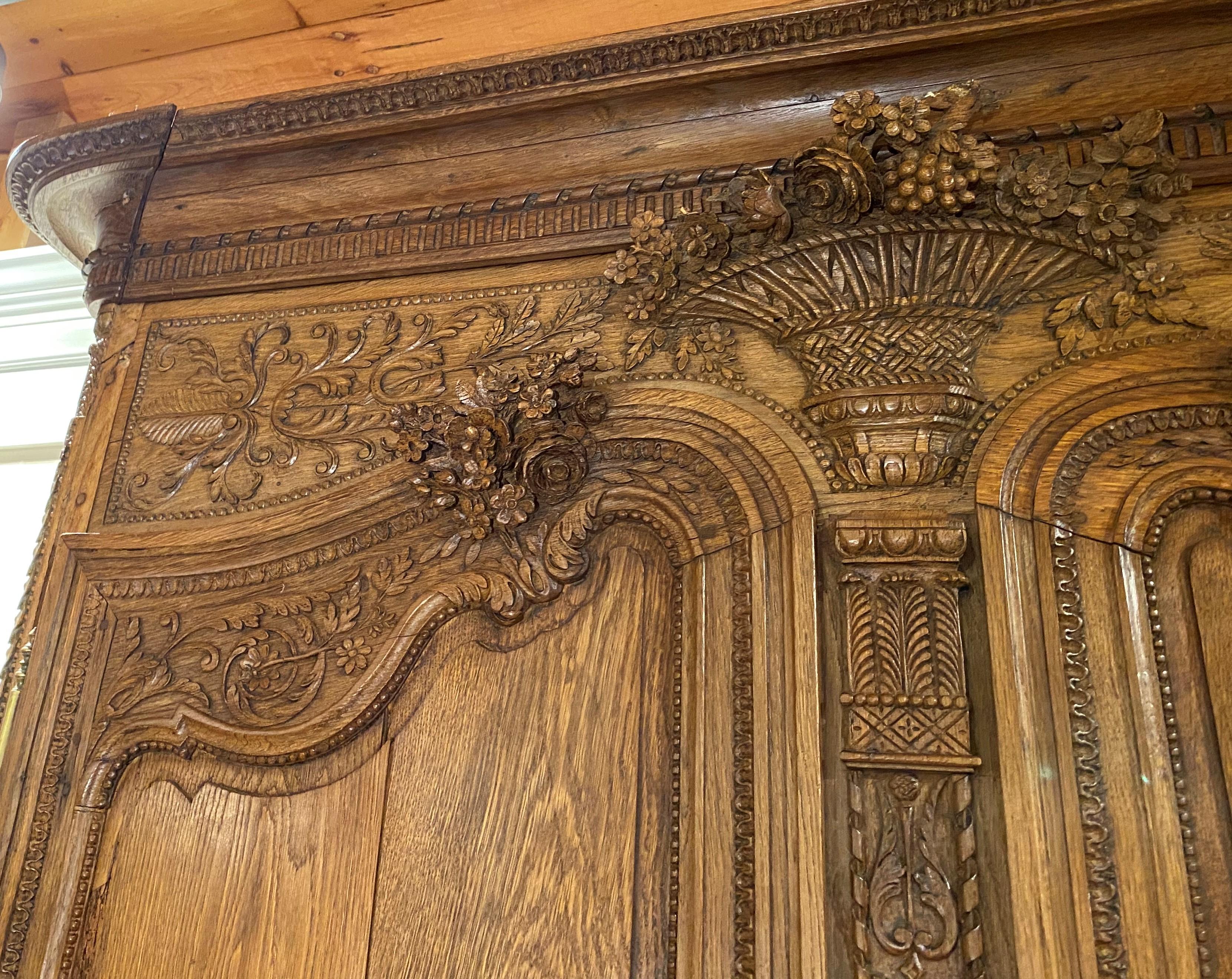 A wonderful French oak armoire, ornately carved with foliate decoration, with molded cornice with stepped out corners surmounting a case with a large central carved urn with flowers, two shaped doors, each with applied foliate decoration at the top,
