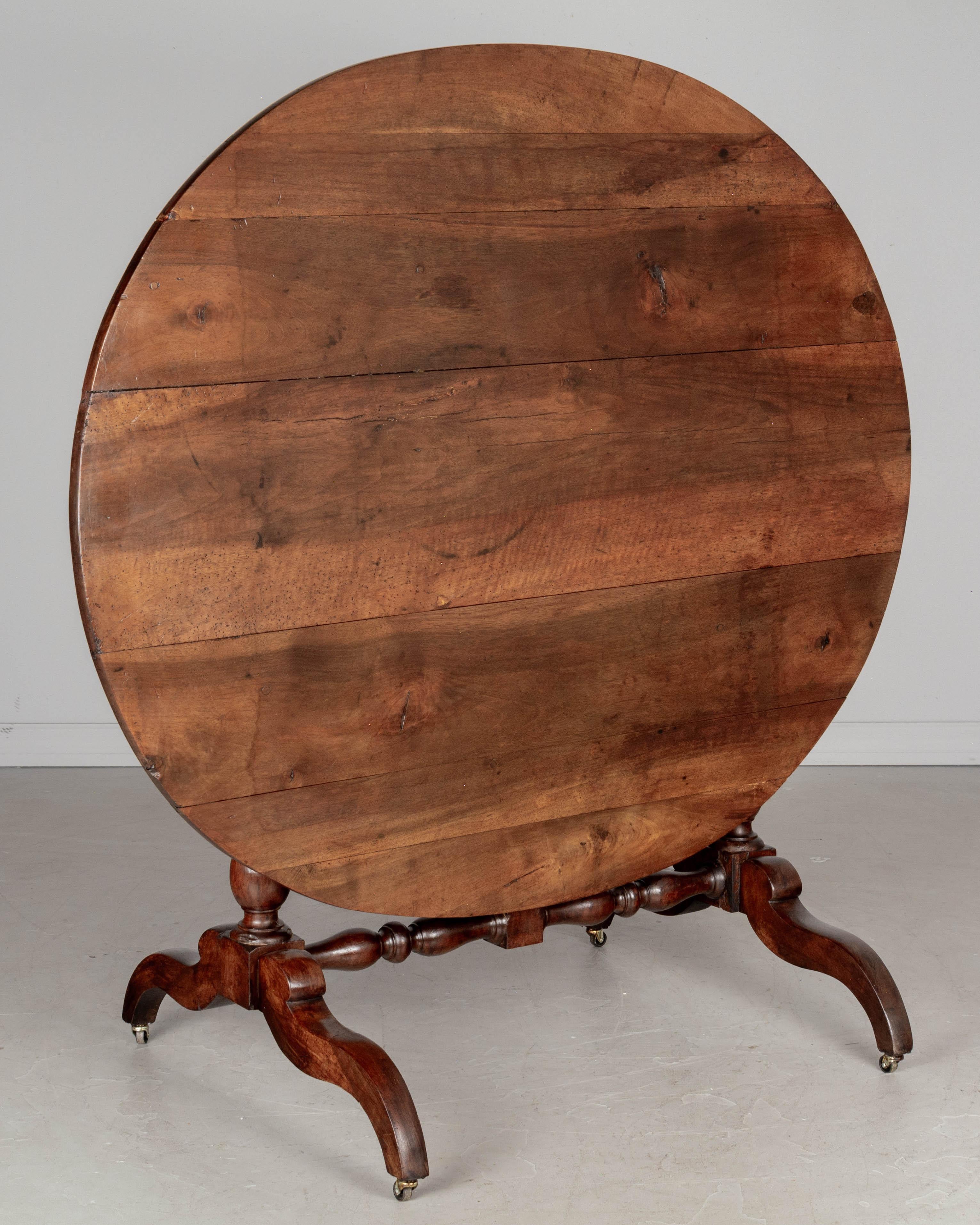 A 19th Century French Louis Philippe style oval wine tasting, or tilt-top table with turned legs and stretcher. Made of solid walnut with nice grain and character. Waxed finish. Wheels have been added and may be removed. Good restored condition.