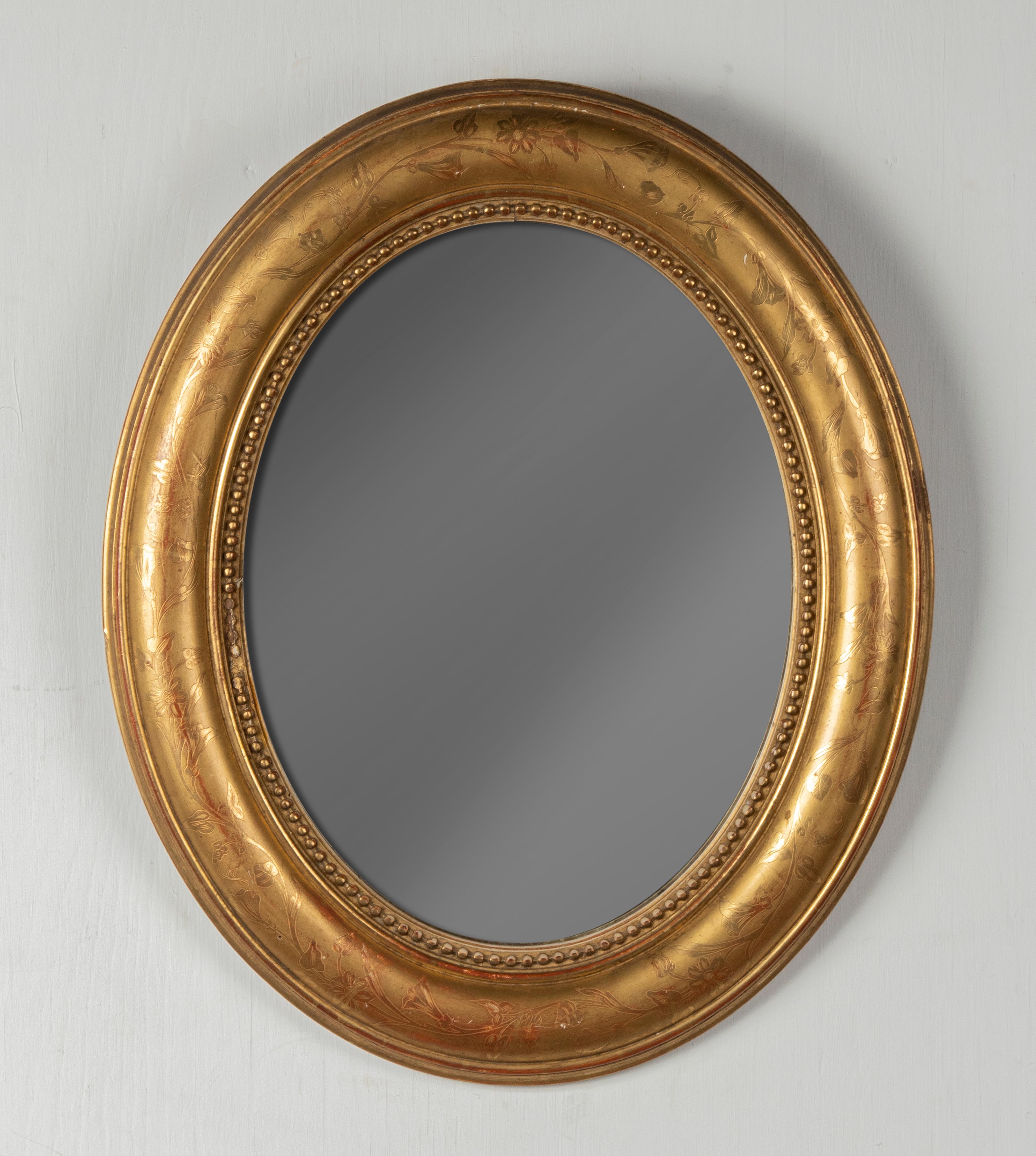 Beautiful antique oval mirror from France. The mirror has a wooden frame, decorated with gesso and gilded with gold leaf. The frame has a decor of fine etched flowers and a pearl rim. The mirror dates from about 1880. The glass is original from the
