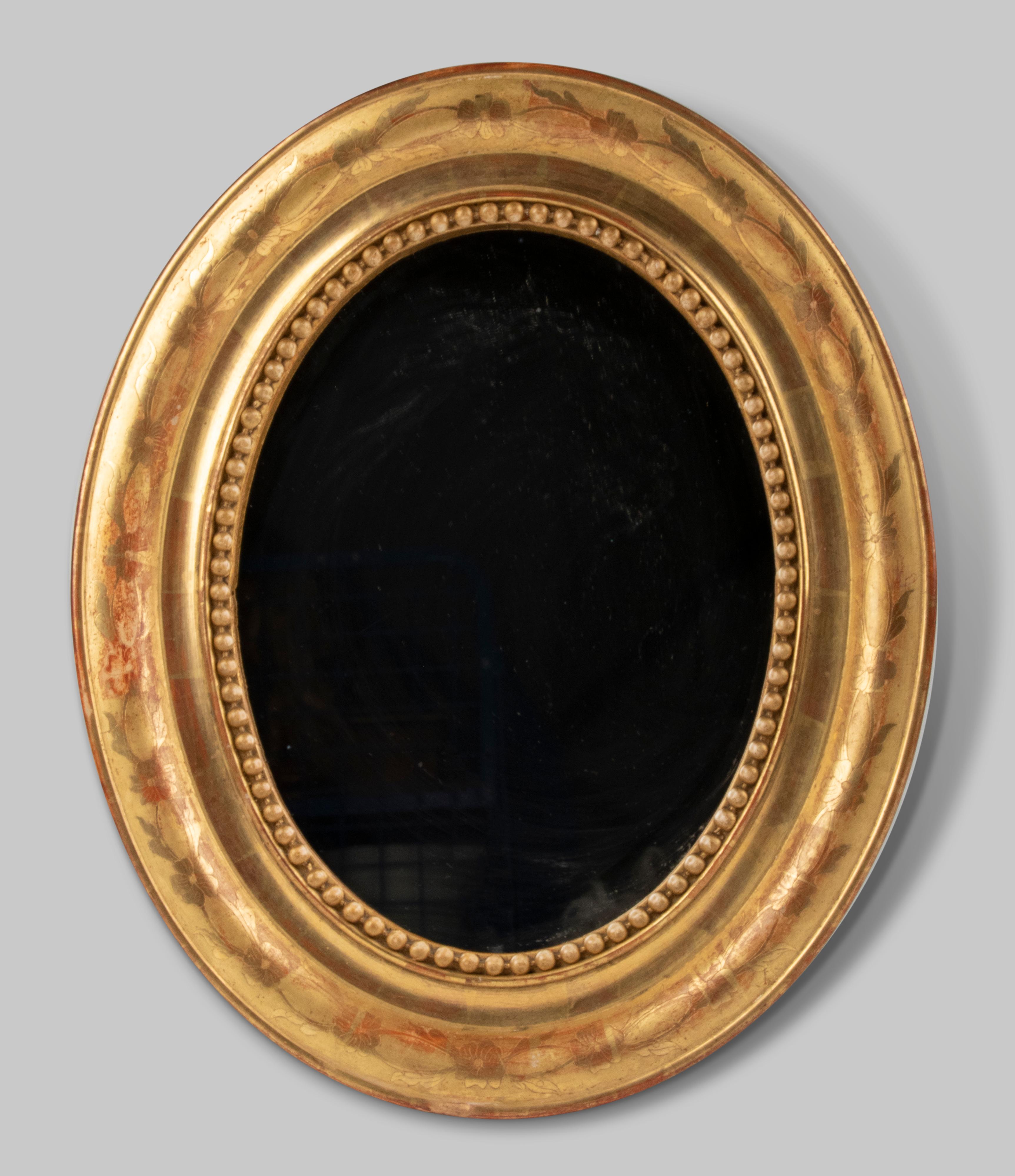 Beautiful antique French oval mirror in Louis Philippe style. It is a small size mirror. The frame is made of wood and plaster and decorated with an etched pattern of flowers. The frame is gilded in red.
This mirror dates from circa 1870-1880 and