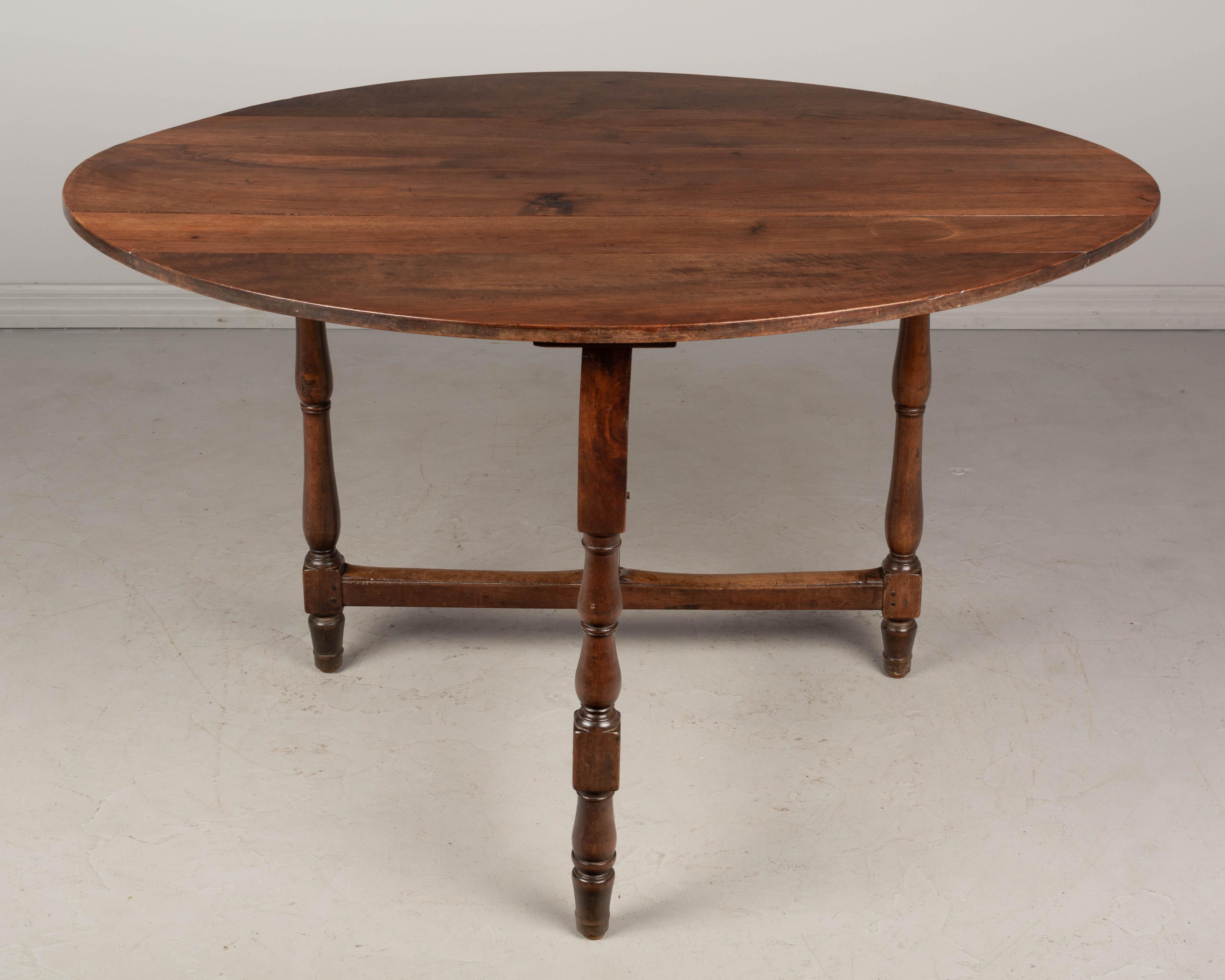 A 19th century French Louis Philippe style oval folding dining table made of solid walnut. Sturdy gate base with three turned legs. Sturdy and well crafted with mortise and tenon joints and pegged construction. Good original condition. Waxed patina.