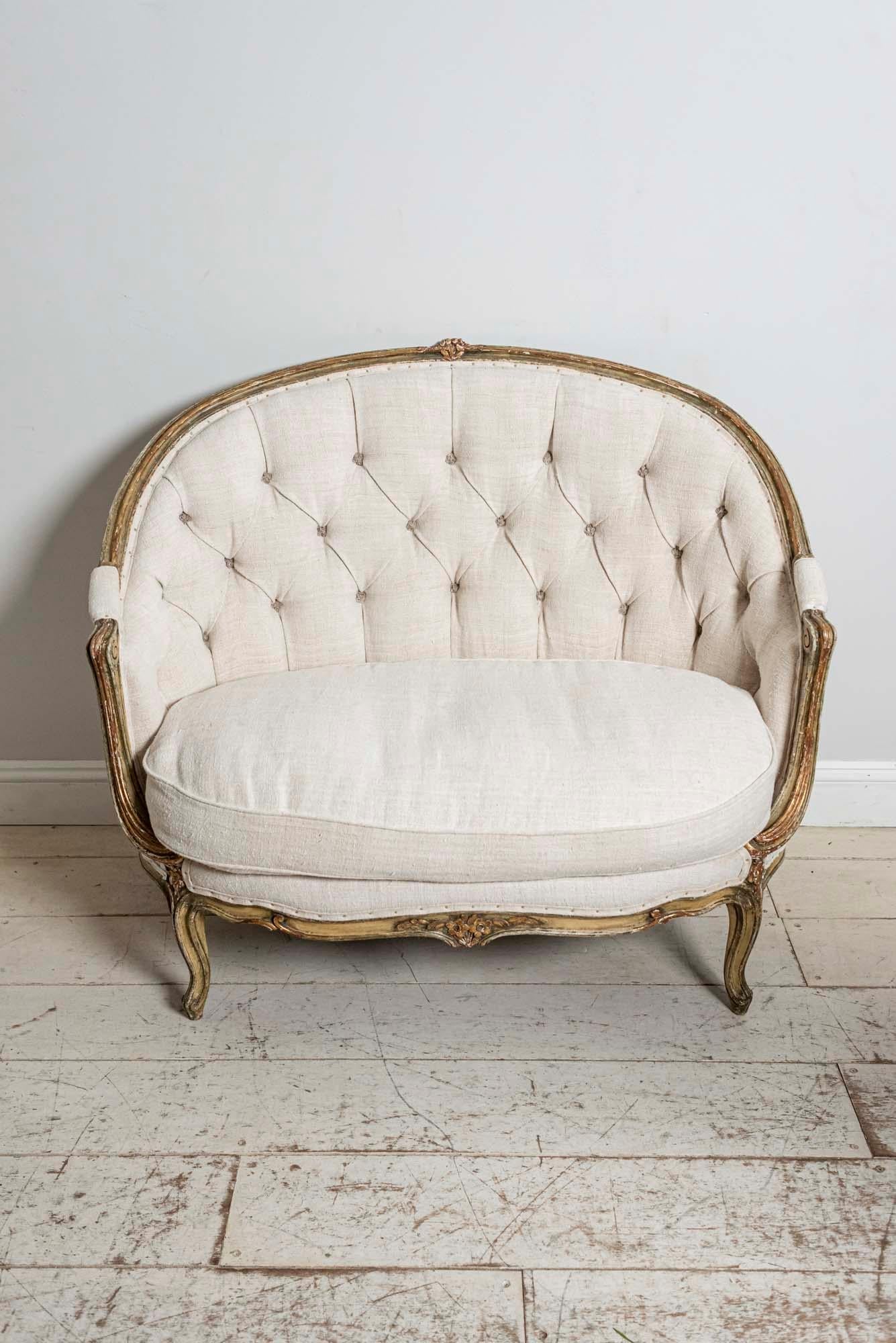 A French 19th century button-backed two seater curved sofa with traces of green and gilt paint to the wooden frame. This wonderful compact sofa features scrolls down the sides and has carved detail of leaves and flowers at the front. It has been