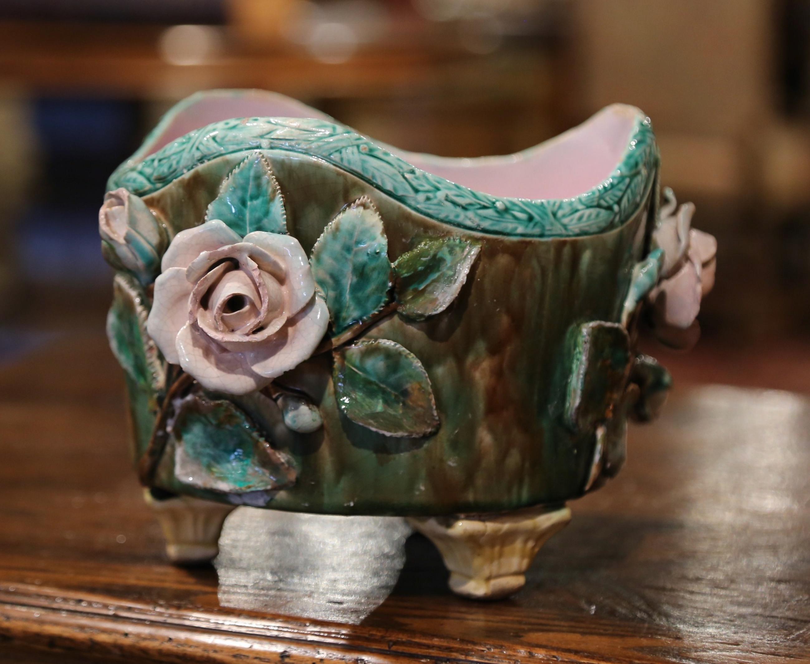 Decorate a table or a console with this colorful, antique Majolica planter. Created in France circa 1880, the sculptural ceramic cachepot stands on three shaped feet; the pot is decorated with hand painted rose flowers and leaf motifs in high