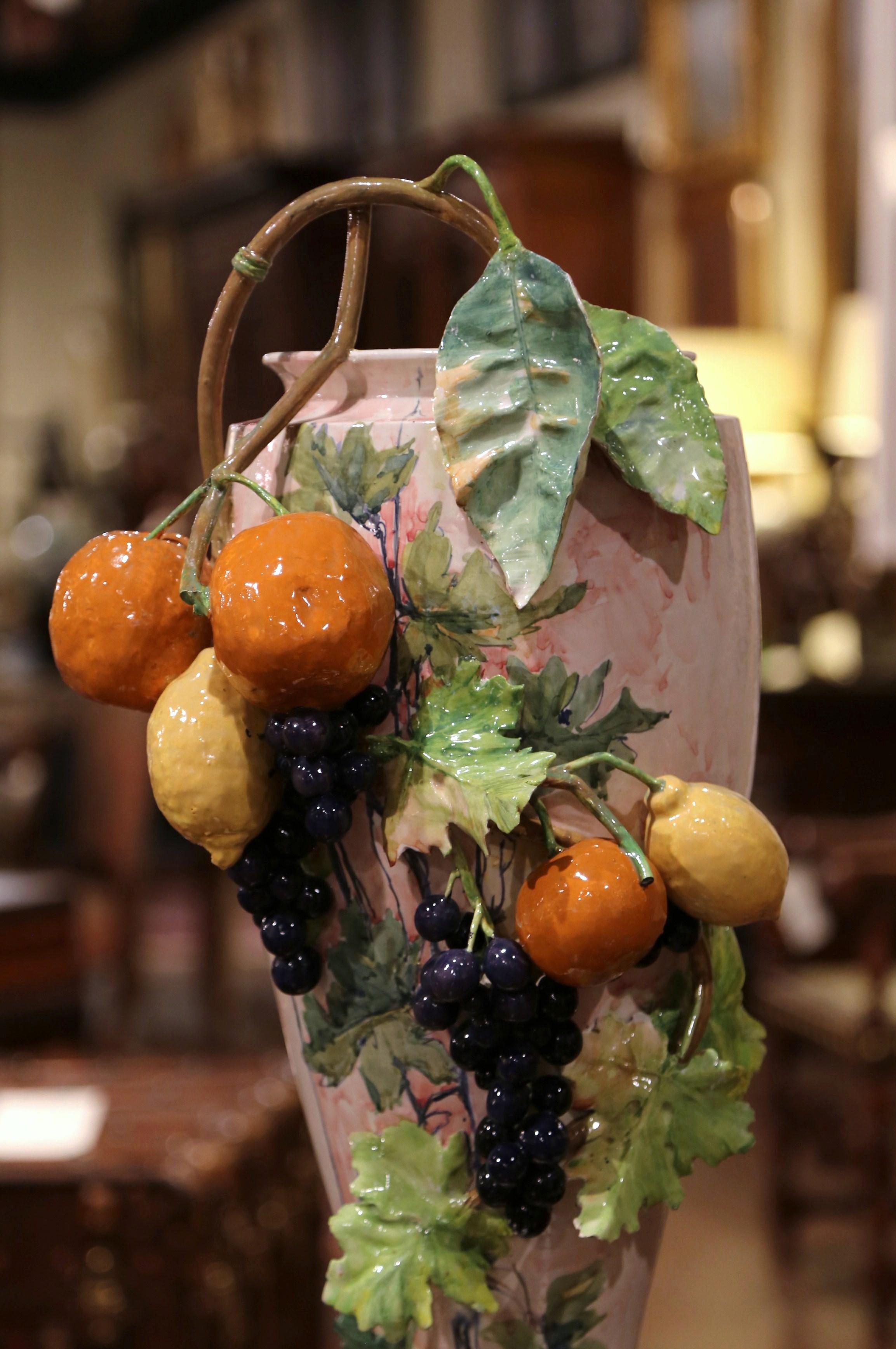 This large, antique hand painted majolica vase was created in France, circa 1890. The tall vase features high relief fruit and leaf decor including grape, oranges, lemons and vine motifs. The colorful vessel is in excellent condition with rich