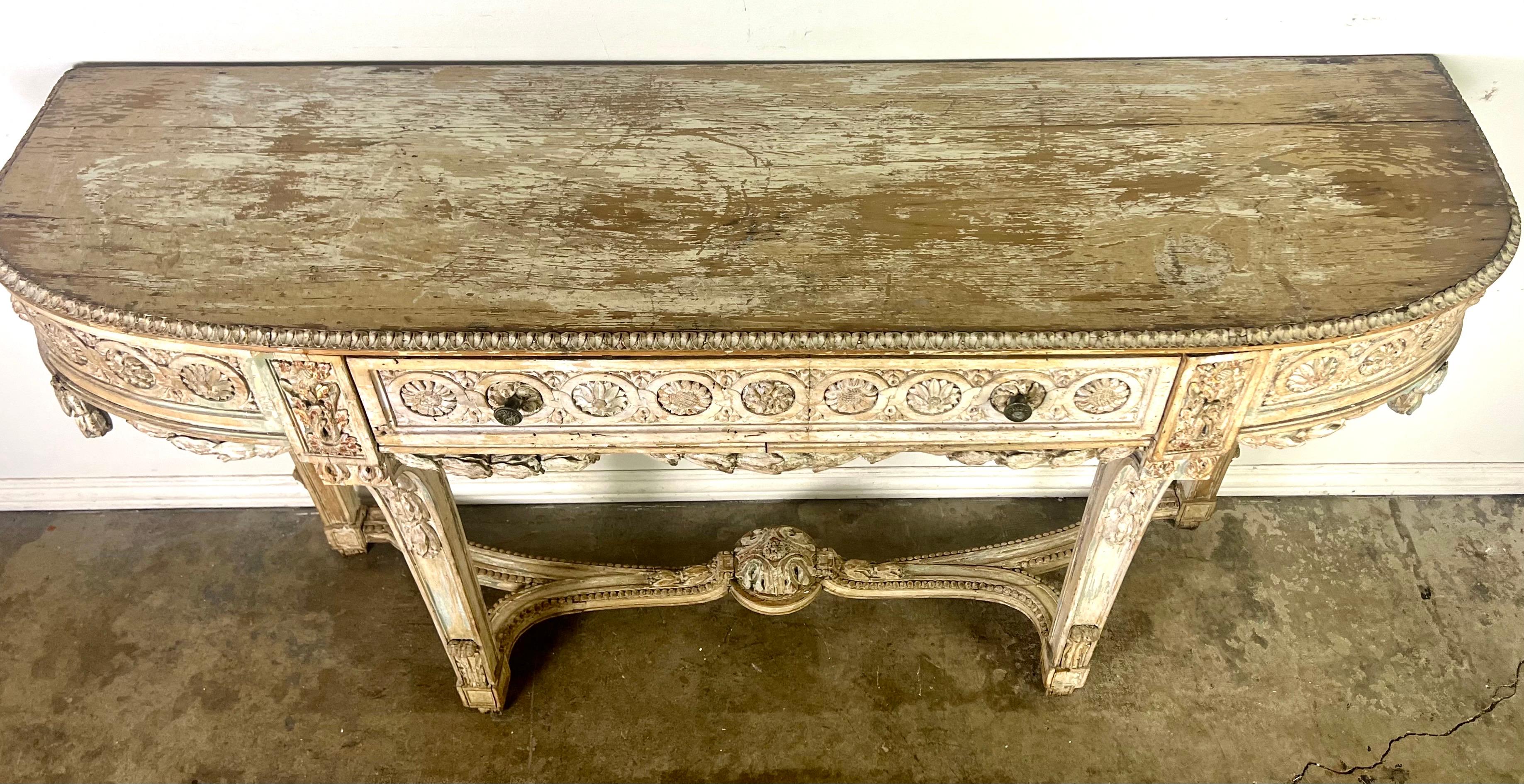 19th century French provincial painted console with hand-carved intricate detailing of garlands, rosettes, and laurel leaf designs. The four carved legs connected by a center stretcher with a cartouche provide both stability and aesthetic appeal. 