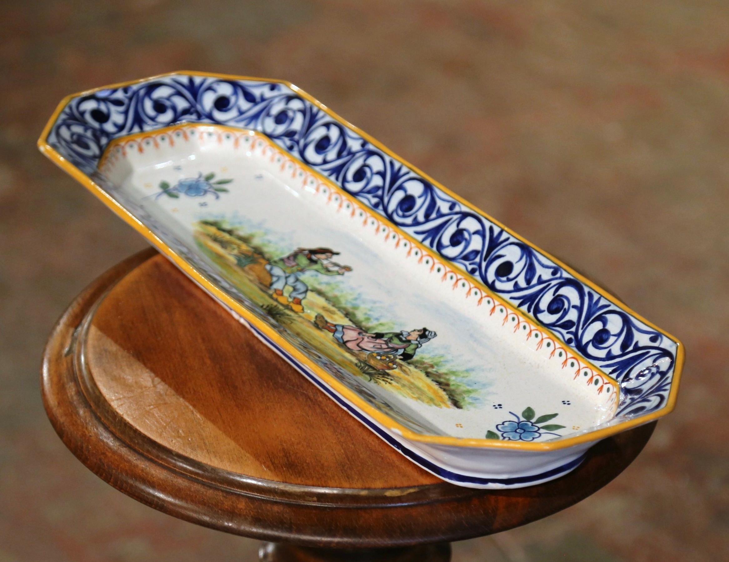 Serve peanuts or chips in this elegant antique dish! Created in Brittany, France circa 1895, the hand painted faience dish is rectangular in shape with cut corners. The serving platter is decorated at the center with a Breton couple in traditional