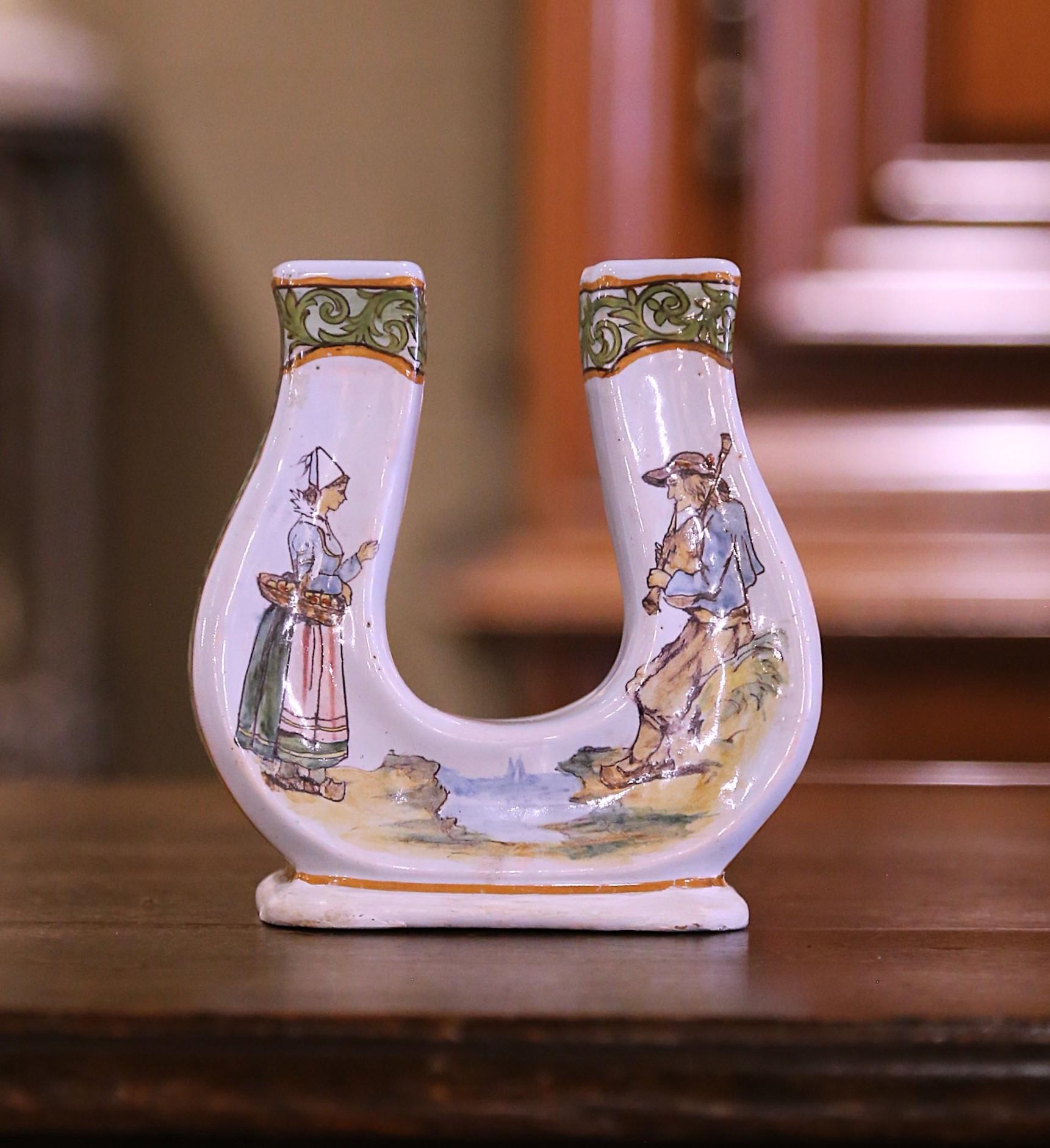 Vesti una mensola con questo bellissimo vaso antico di Porquier-Beau. Realizzato a Qimper, in Francia, intorno al 1895, questo vaso in maiolica a forma di ferro di cavallo presenta una caratteristica forma a lira decorata con una scena tipica