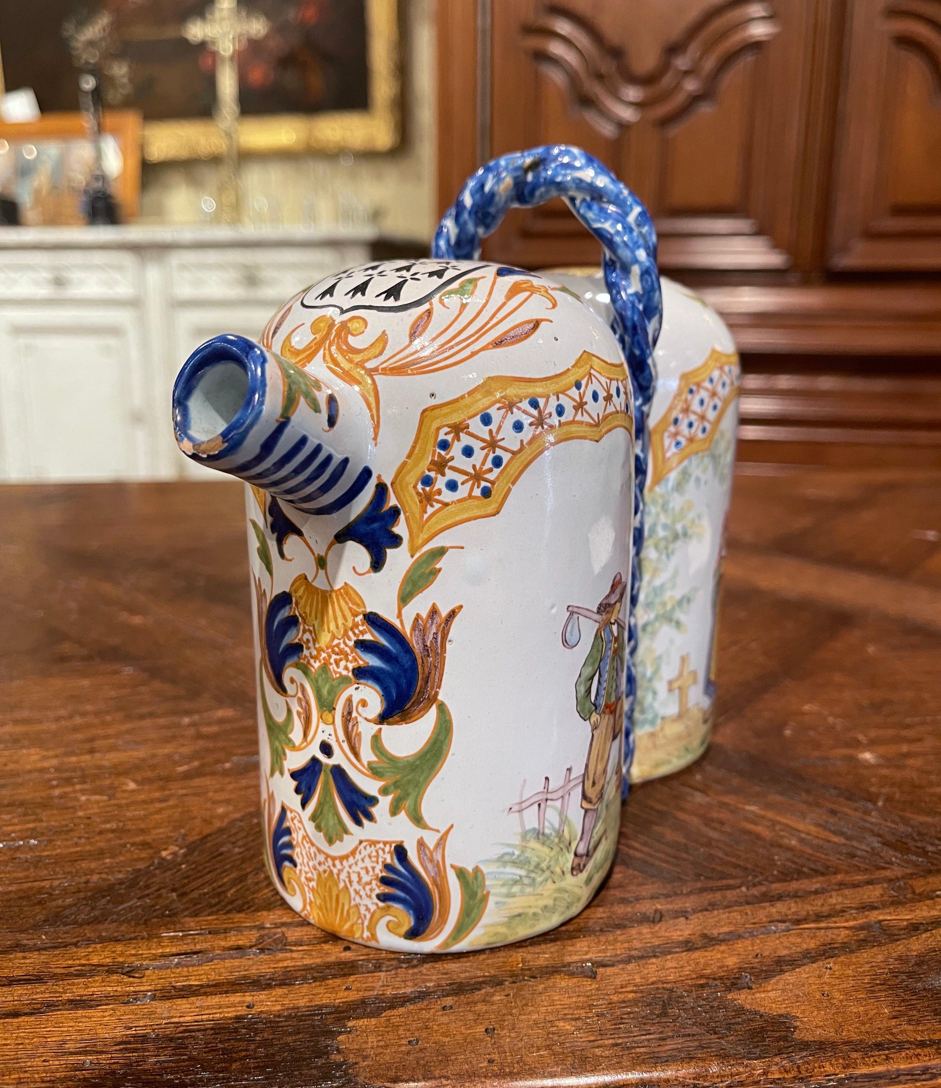 Decorate a kitchen counter or a shelf with this elegant antique conjoined double pitcher. Created in Brittany, France circa 1895, the hand painted ceramic container with center rope twist handle and double spouts, is decorated with Breton men