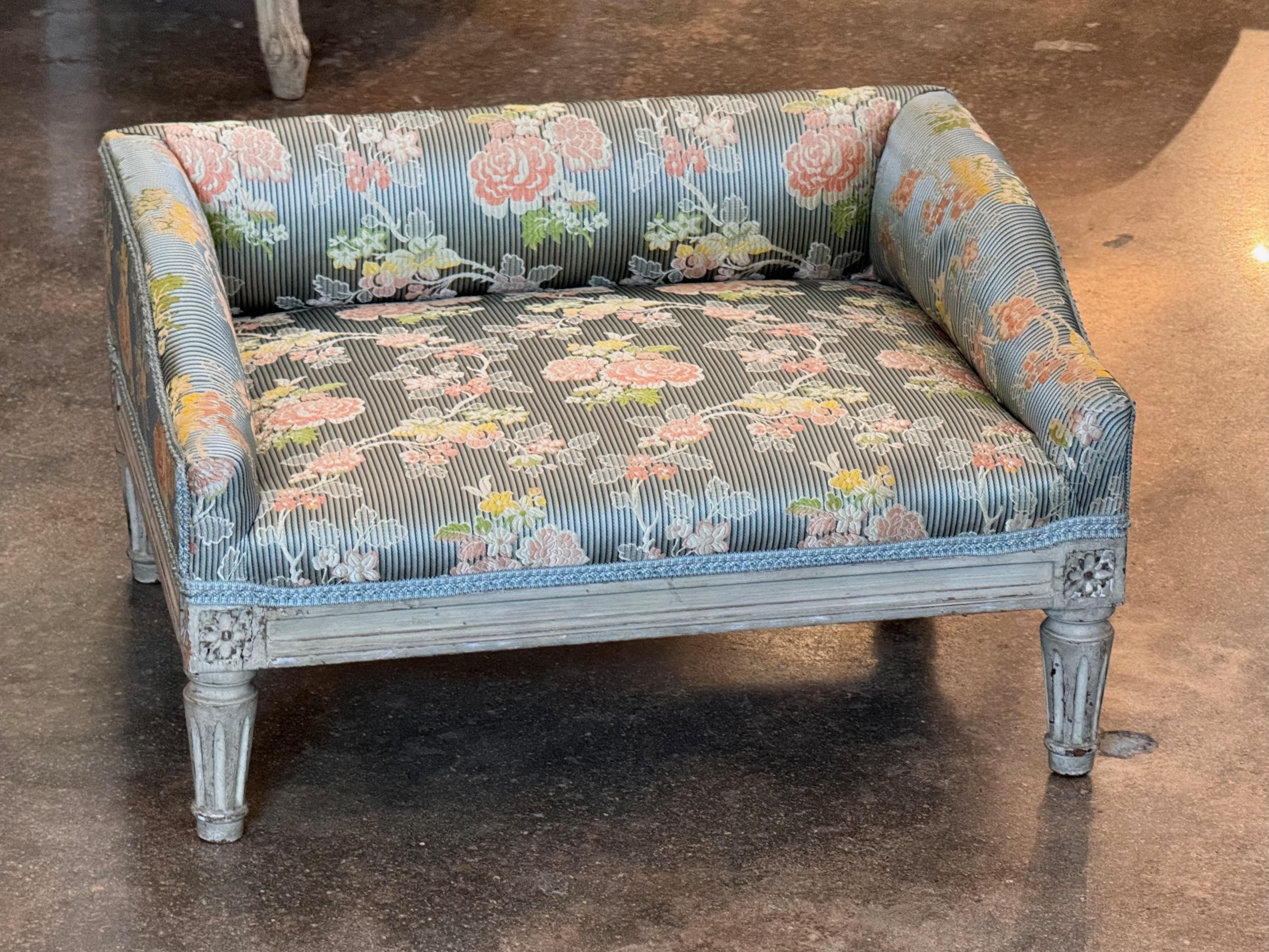 Charmanter französischer Fußhocker aus dem 19. Jahrhundert mit geschnitzten Beinen und floralen Details, bemalt in sanften Grautönen. Das mit einem floralen Vintage-Stoff auf klassisch gestreiftem Grund gepolsterte Stück spiegelt den Einfluss des