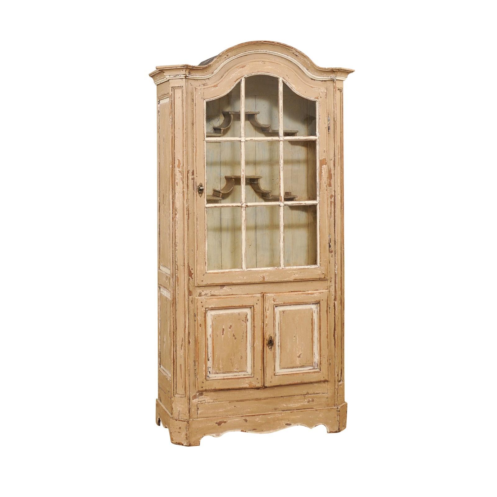 A French painted vitrine cabinet from the 19th century with carved bonnet top, glass door in the upper section and small double doors in the lower one. This French painted vitrine cabinet, originating from the 19th century, seamlessly blends