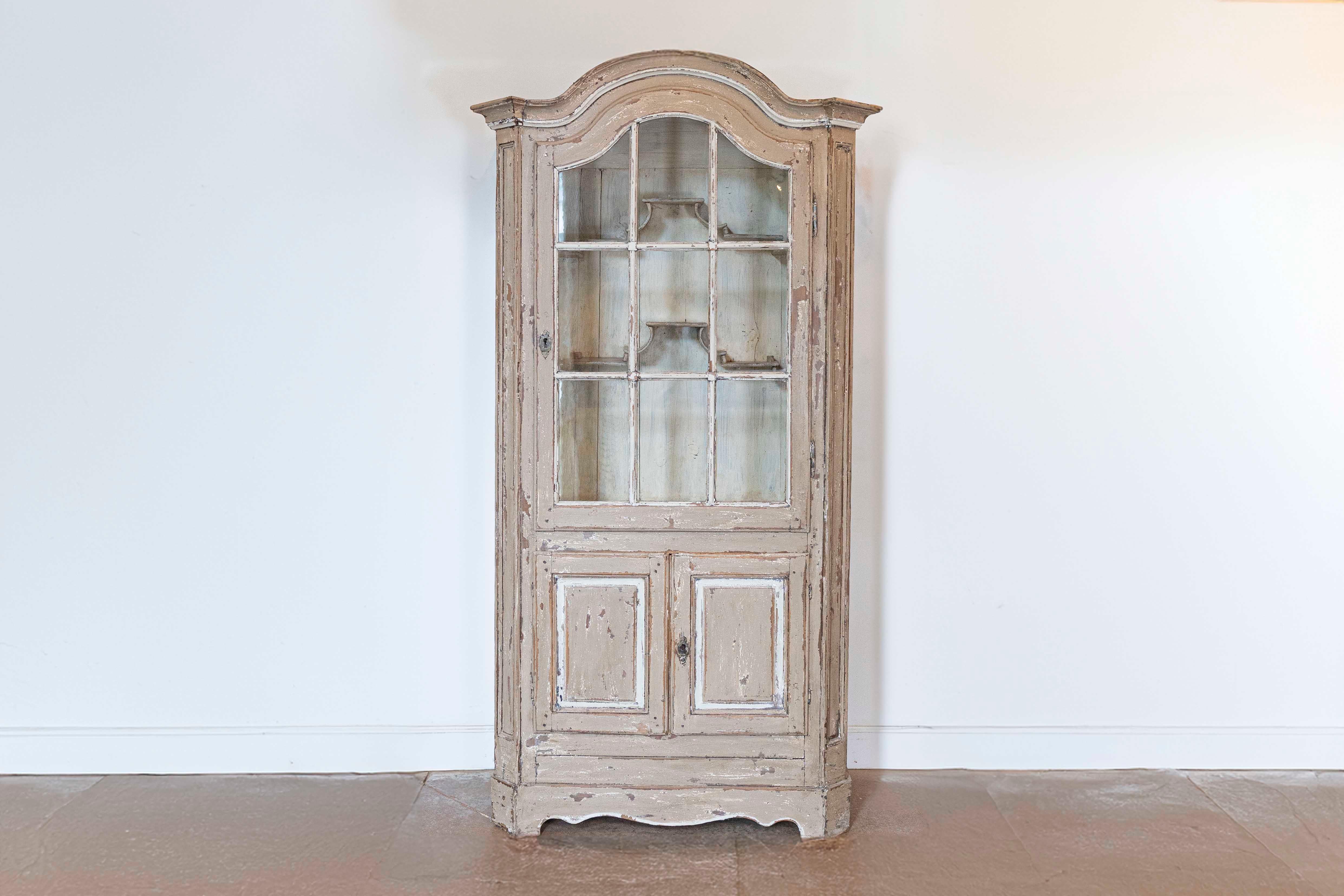A French painted vitrine cabinet from the 19th century with carved bonnet top, glass door in the upper section and small double doors in the lower one. This French painted vitrine cabinet, originating from the 19th century, seamlessly blends