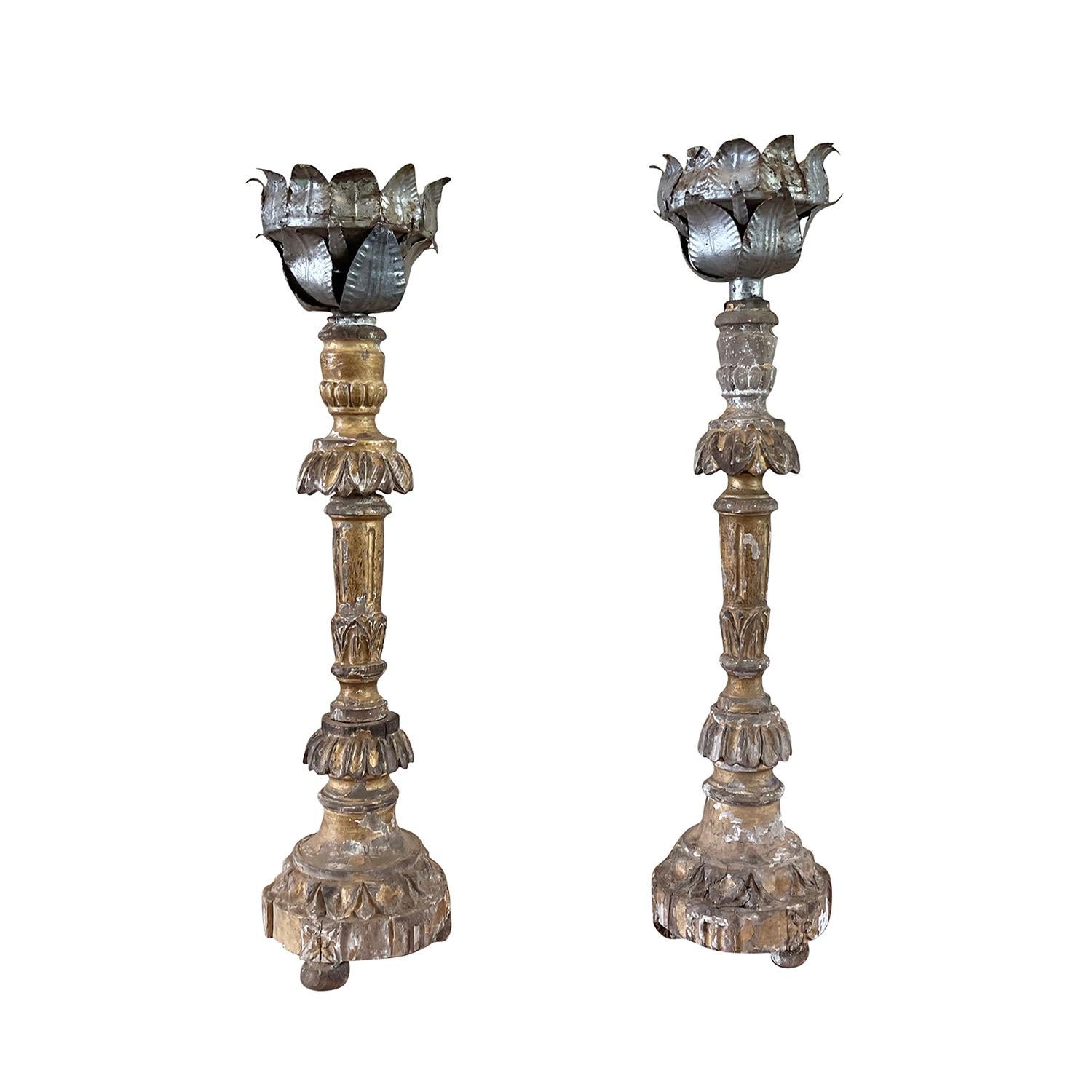 An antique French pair of early 19th Century candle holders on tripod base, carved out of Pinewood with acanthus leaf décor. Original polychrome silver gold patina, in good condition. Topped with hand crafted abundantly adorned metal cup with