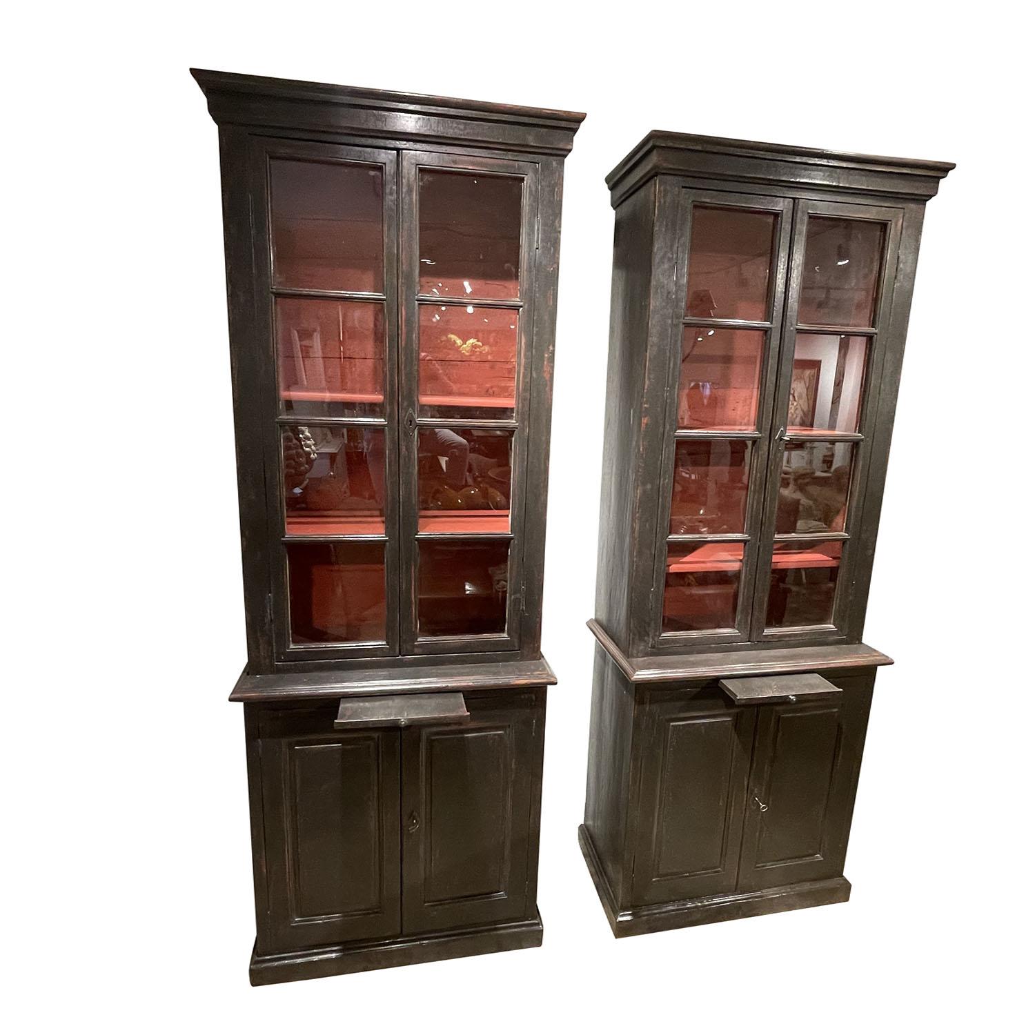 An antique pair of French Provincial black bookcases or library cabinets made of hand crafted painted Sprucewood, in good condition. The upper part is composed with two glass display doors and the interior contains two shelves. The lower part of the