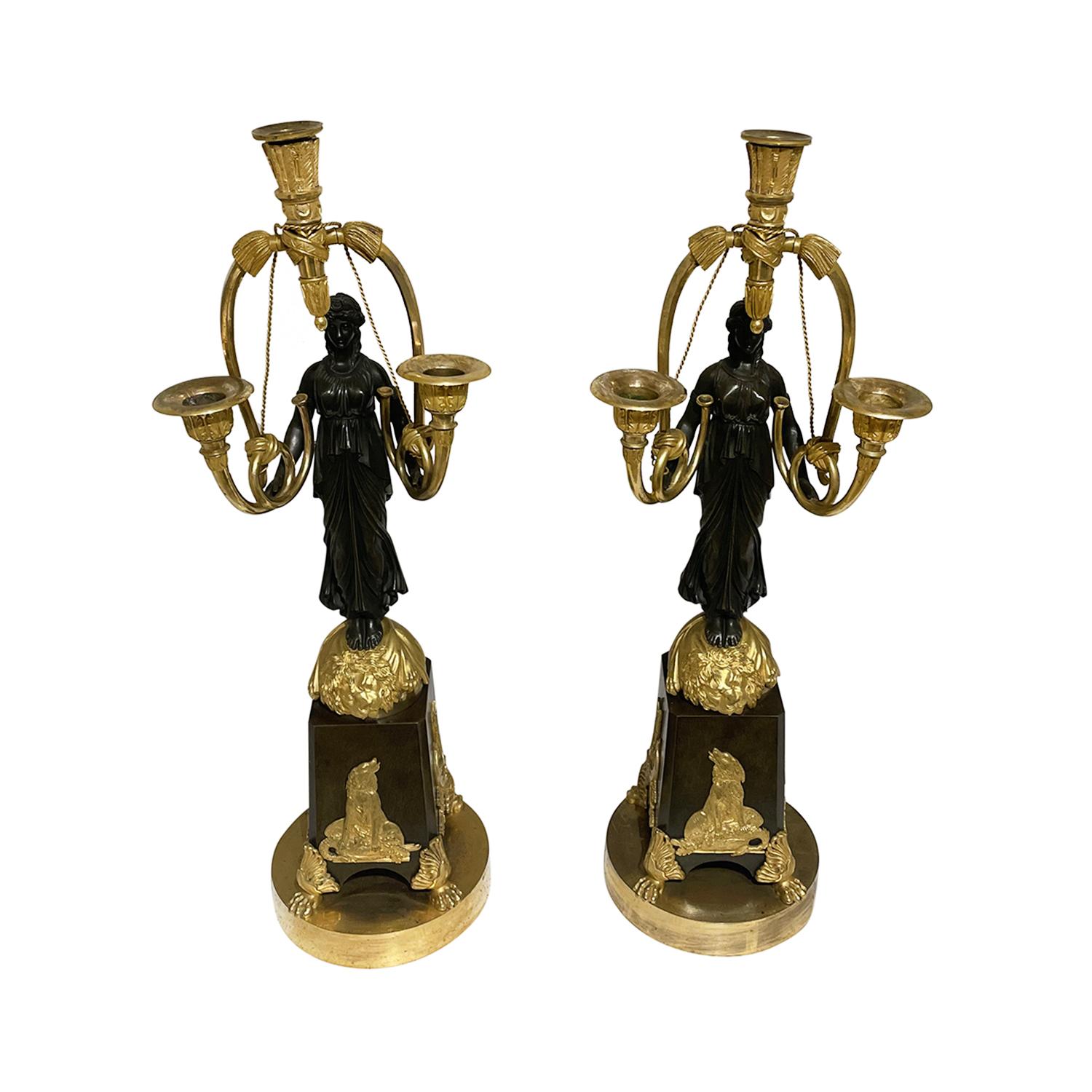 A gold-black, antique French pair of girandoles made of hand crafted gilded bronze attributed to Friedrich Bergenfeldt, in good condition. Each of the detailed Parisian candle holders are composed with a female warrior, particularized with hunting