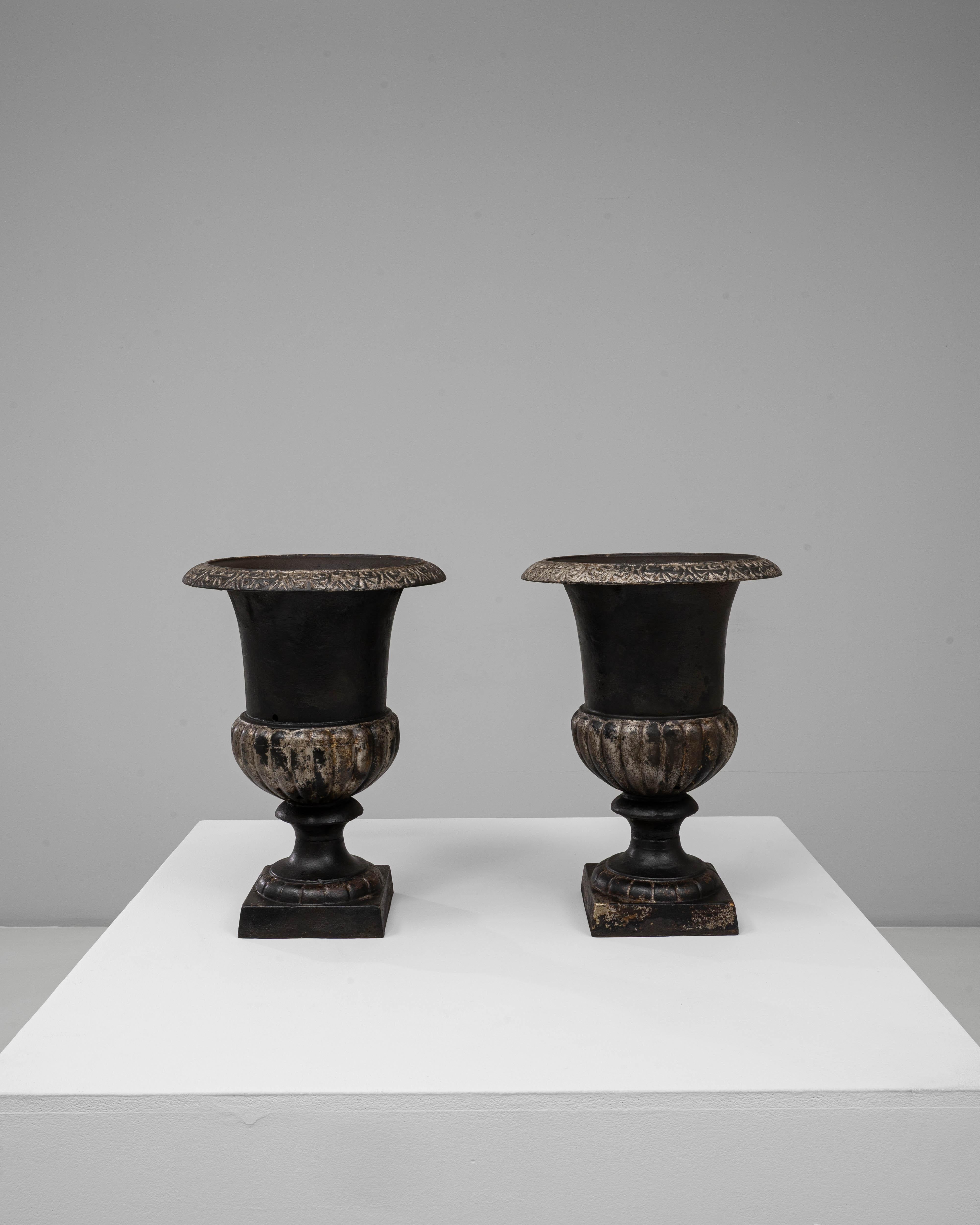 Questa coppia di fioriere in ghisa di Campagna, risalente al XIX secolo, è un esempio di design classico per il giardino e di maestria artigianale duratura. Ciascuna urna presenta un bordo svasato con intricati dettagli foliati, un corpo a coste e