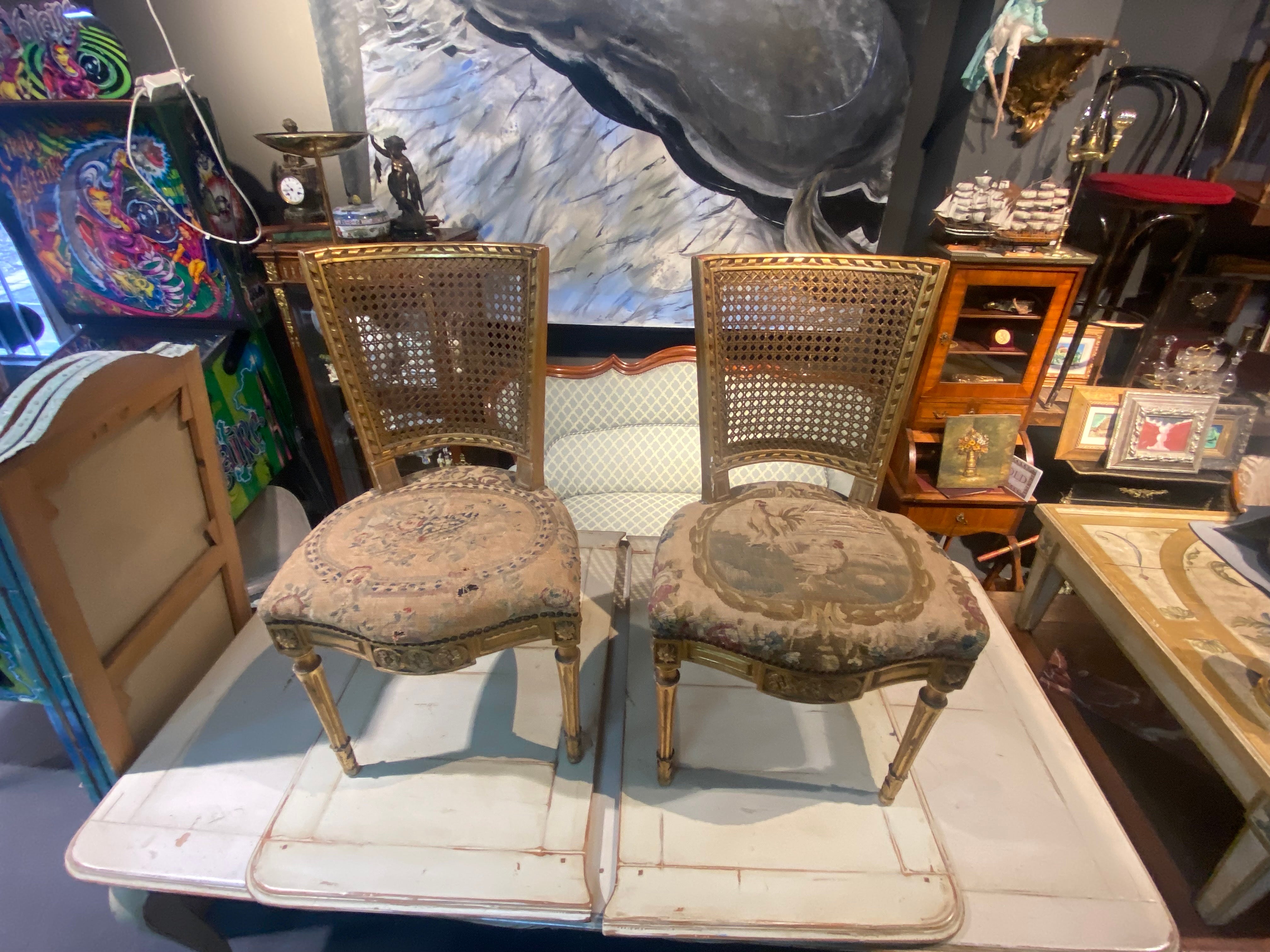 Lovely pair of gild wood side chairs still wearing authentic tapestry upholstery, which is quite used and better be replaced. The chairs are having cane backs in good condition and are very stable. The style is typical for Louis XVI period and there