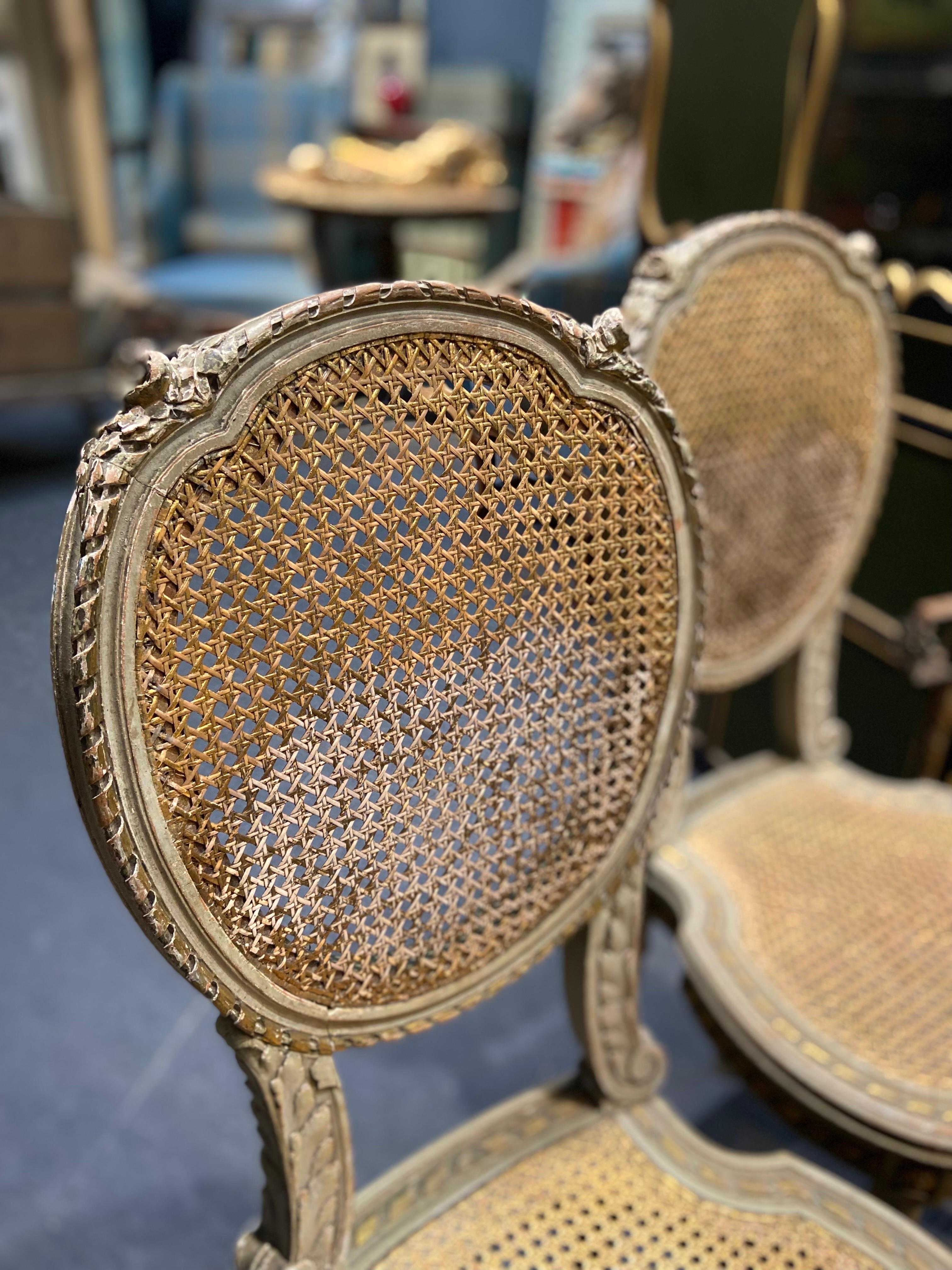 19th century French pair of hand-painted in light green wooden chairs with delicate oval cane backs and seats in Louis XVI style. Both are hand carved and decorated with roses and leaves and are in good condition. There is just a small damage of the