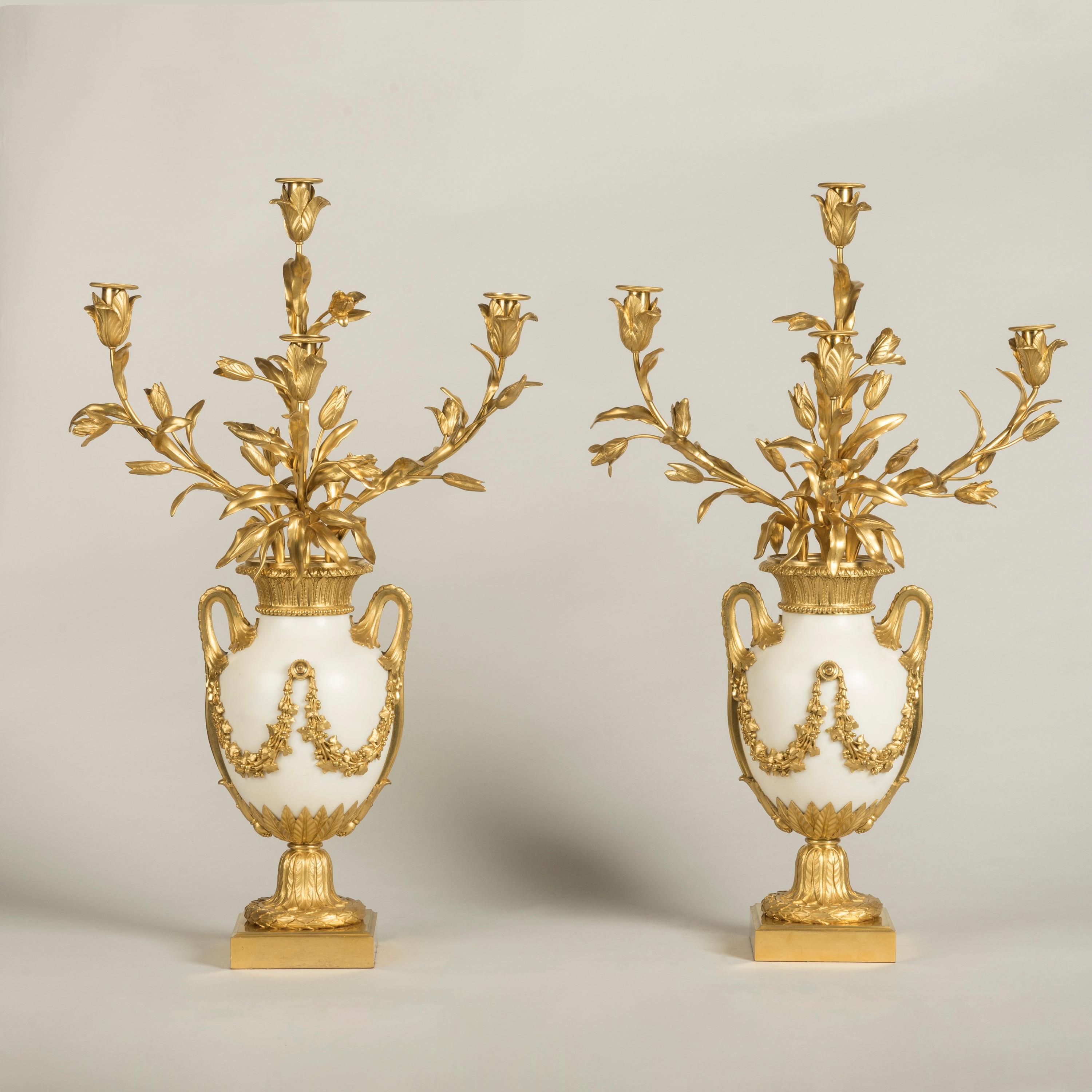 A Fine Pair of Ormolu-Mounted Candelabra 
in the Louis XVI Manner

Constructed from Carrara marble with mercury gilded mounts, the vases are supported on square bases with laurel-wreathed socles; the marble ovoid bodies with ormolu foliate twinned