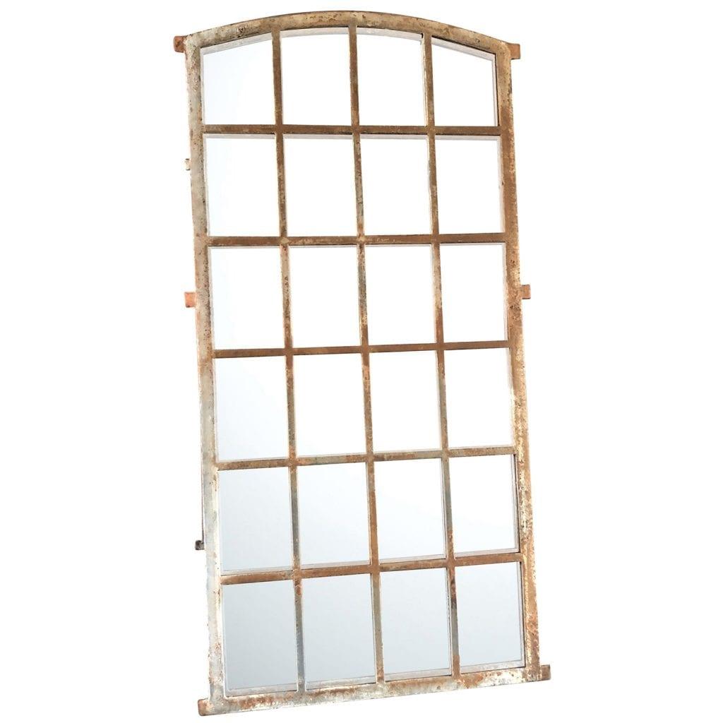 An antique pair of 24- field mirrored French Orangerie windows with a cast iron frame and a slightly arched top, in good condition. Metal aged frame and newly inserted mirror panels. The antique wall décor represents the Rococo time period. Wear