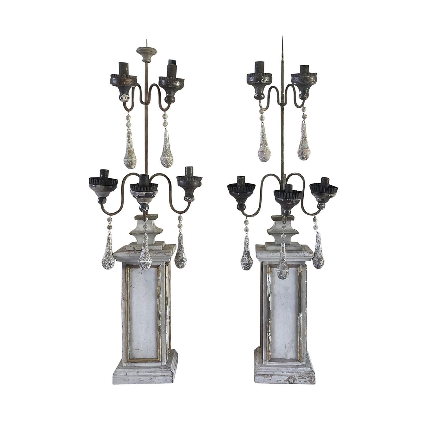 Une paire de chandeliers français anciens en bois de pin travaillé à la main, en particulier dans une finition lavée en blanc, en bon état. La haute base élancée supporte les quatre bâtons de bougie insérés. Des serpentins décoratifs en bois