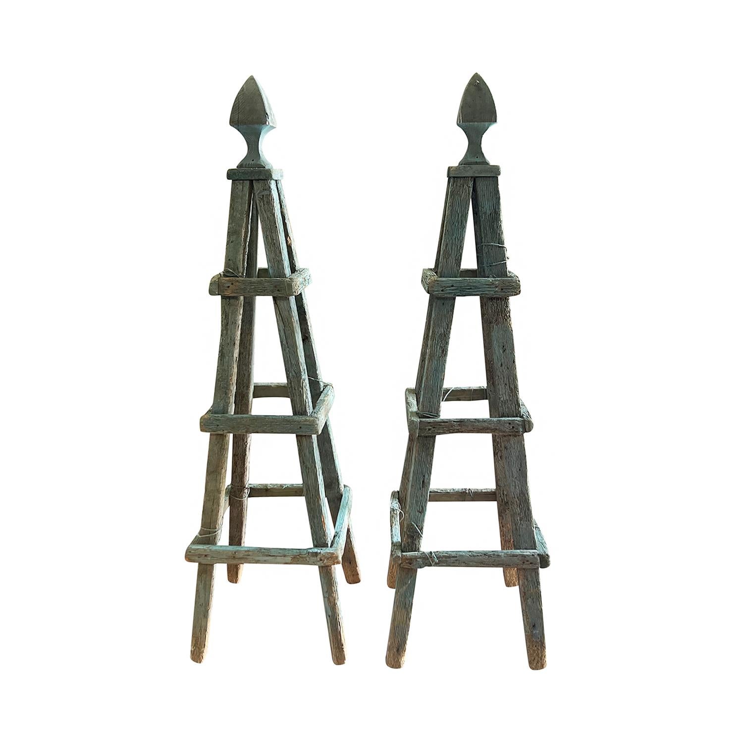 An antique pair of tall treillis obelisks in Versailles green topped by pointed finials, in good condition. These antique hand crafted painted Pinewood obelisks have multiple layers of old paint and therefore have a lot of character and presence. A