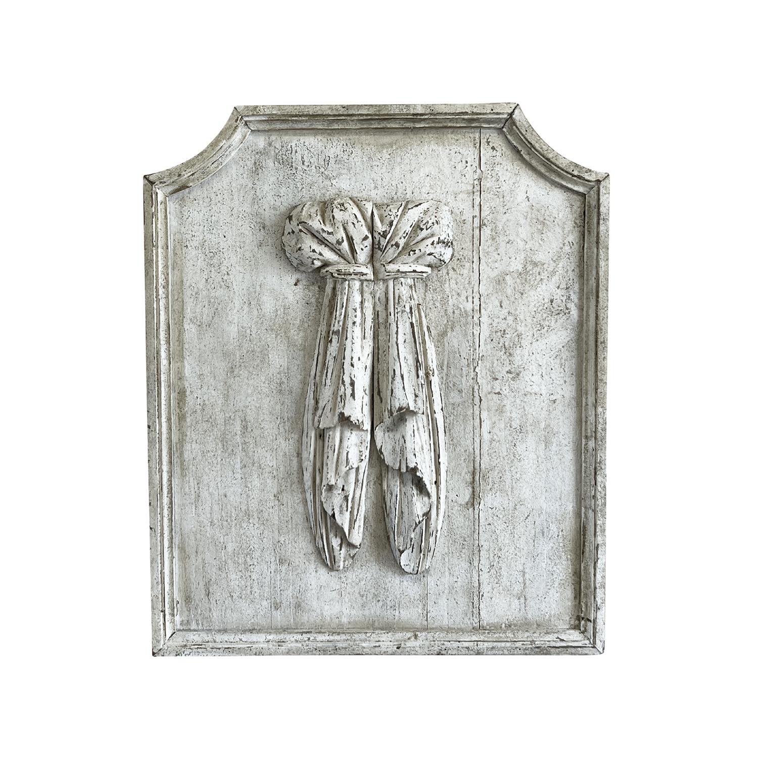An antique French Provincial pair of vertical decorative wall panels made of hand crafted Pinewood, depicting bundles of tied cloth, in good condition. The reliefs have a light-grey white original patina and the top corners of the beveled frames