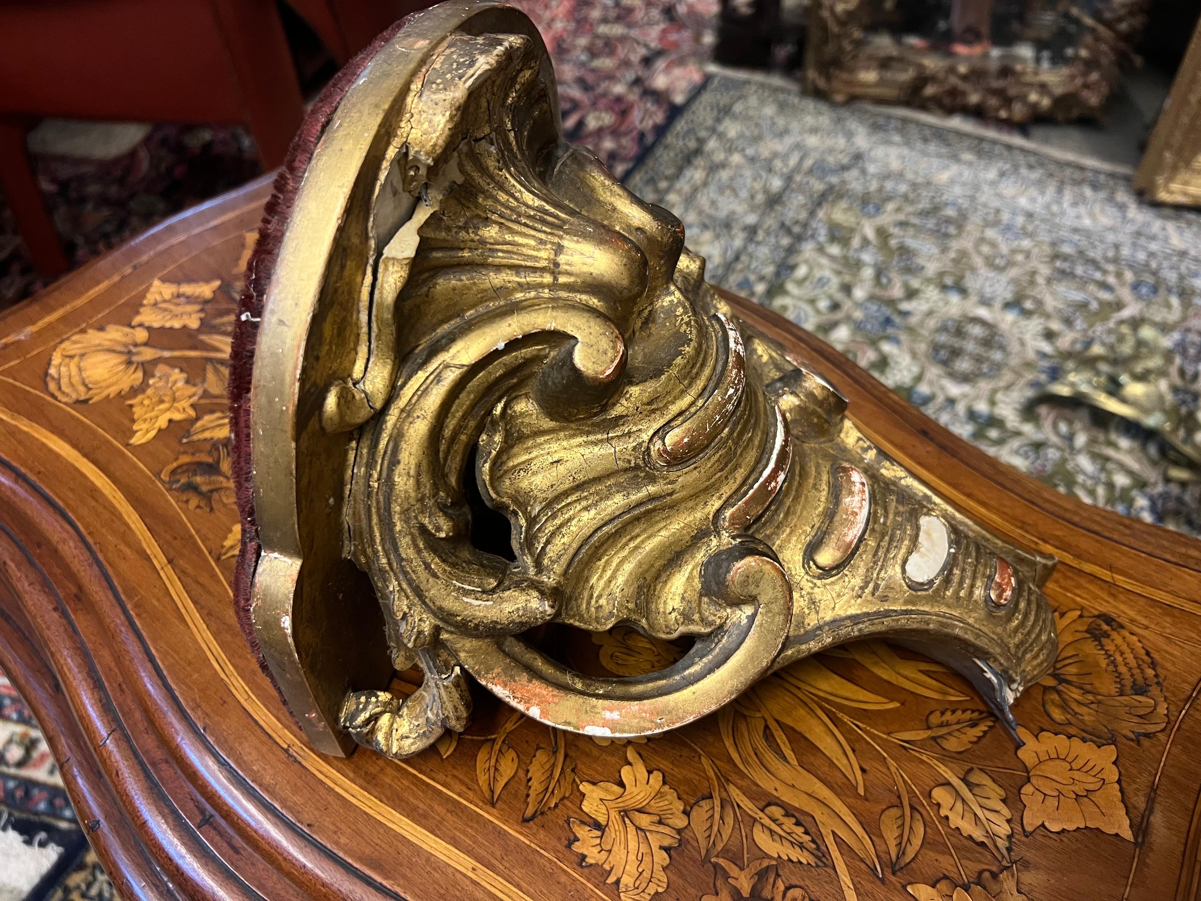 19th Century French small gilt wood hand carved wall mounted console in Rococo style. It has an oval shape and symmetrical decoration and ornaments in good authentic condition with no restorations made. The top was once covered with red velvet that